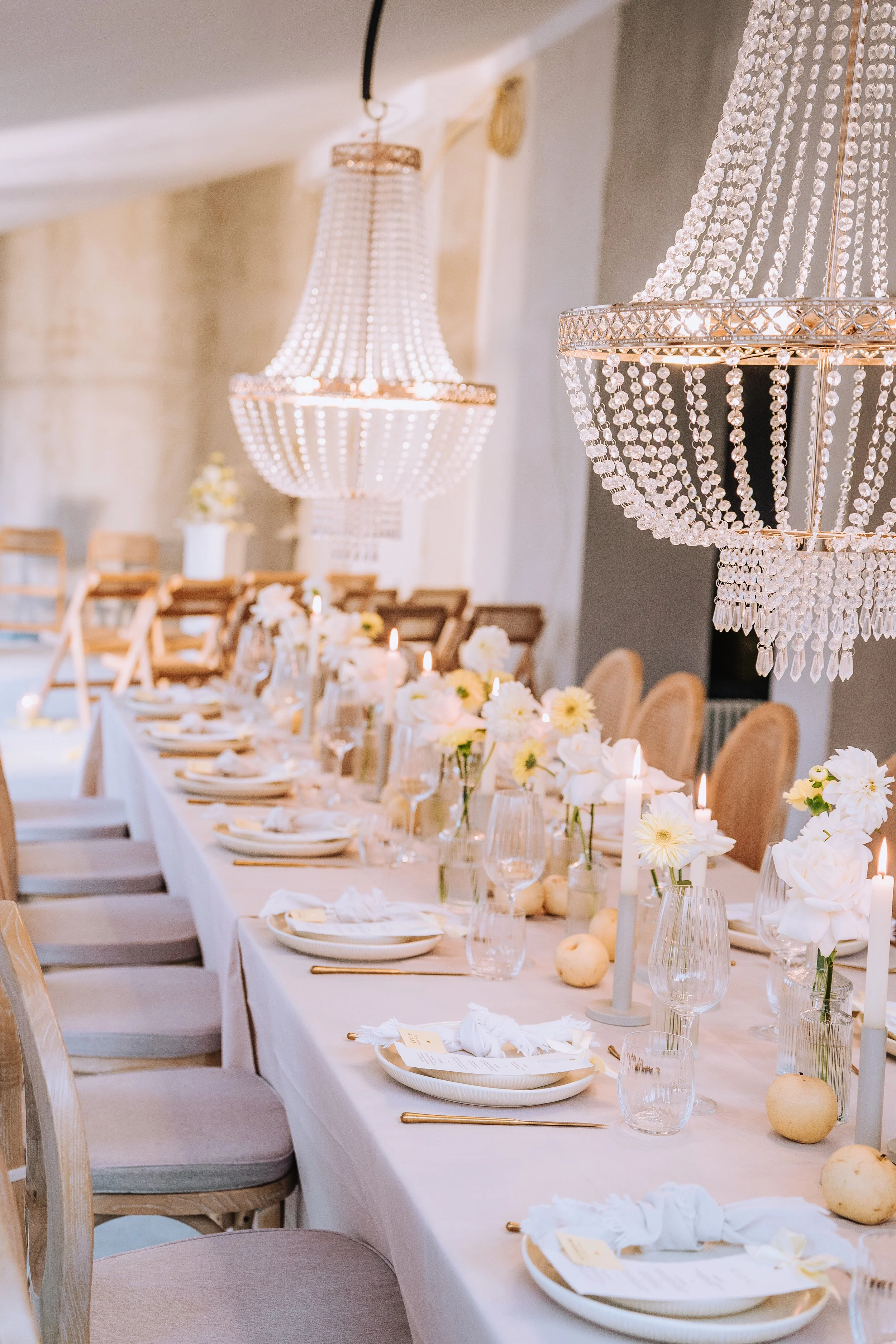 Festlich gedeckter Esstisch mit weißen Blumen, Kerzen und Kristallleuchtern in einem eleganten Raum.