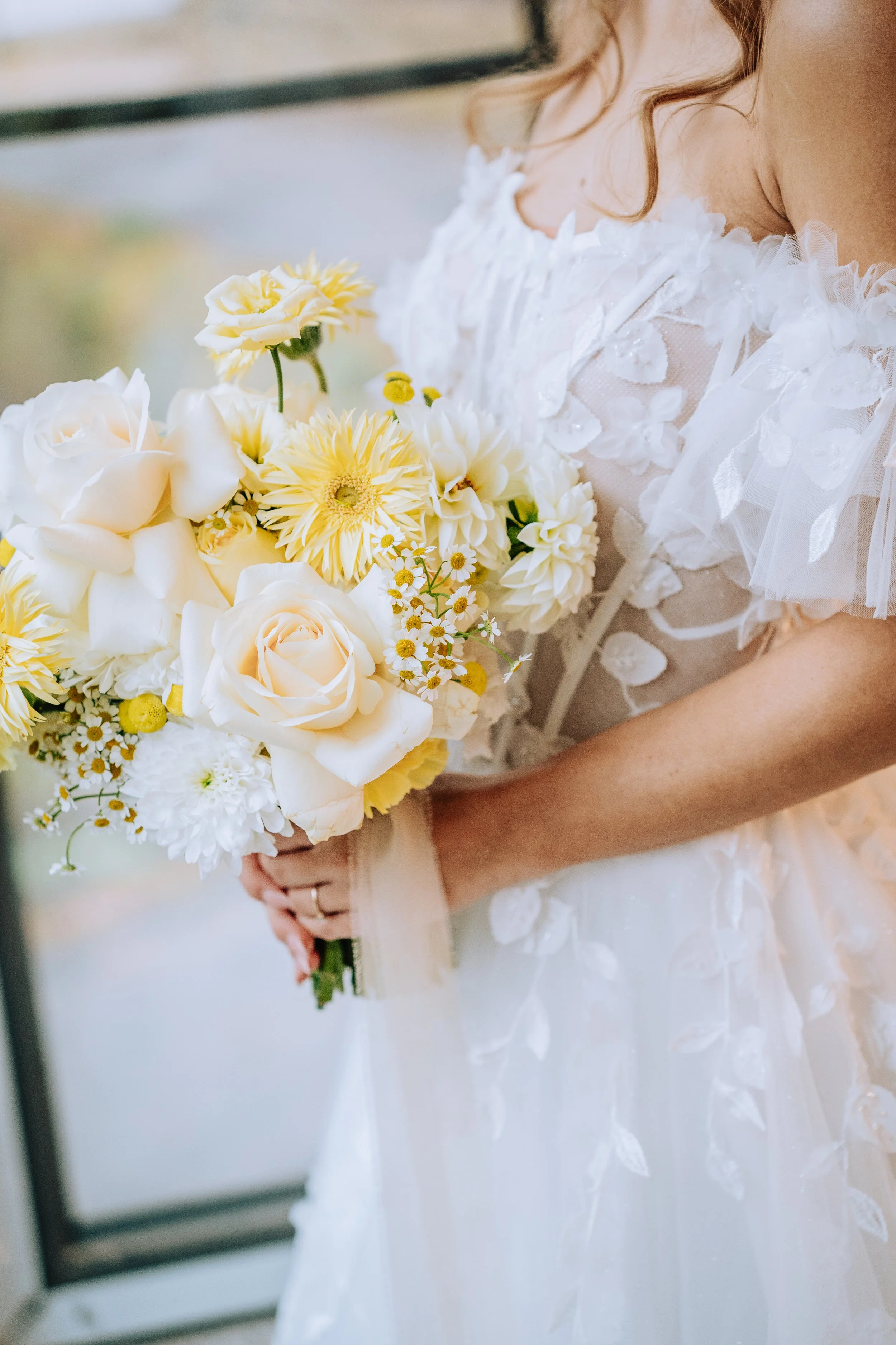 Braut hält einen Hochzeitstrauß mit weißen und gelben Blumen.