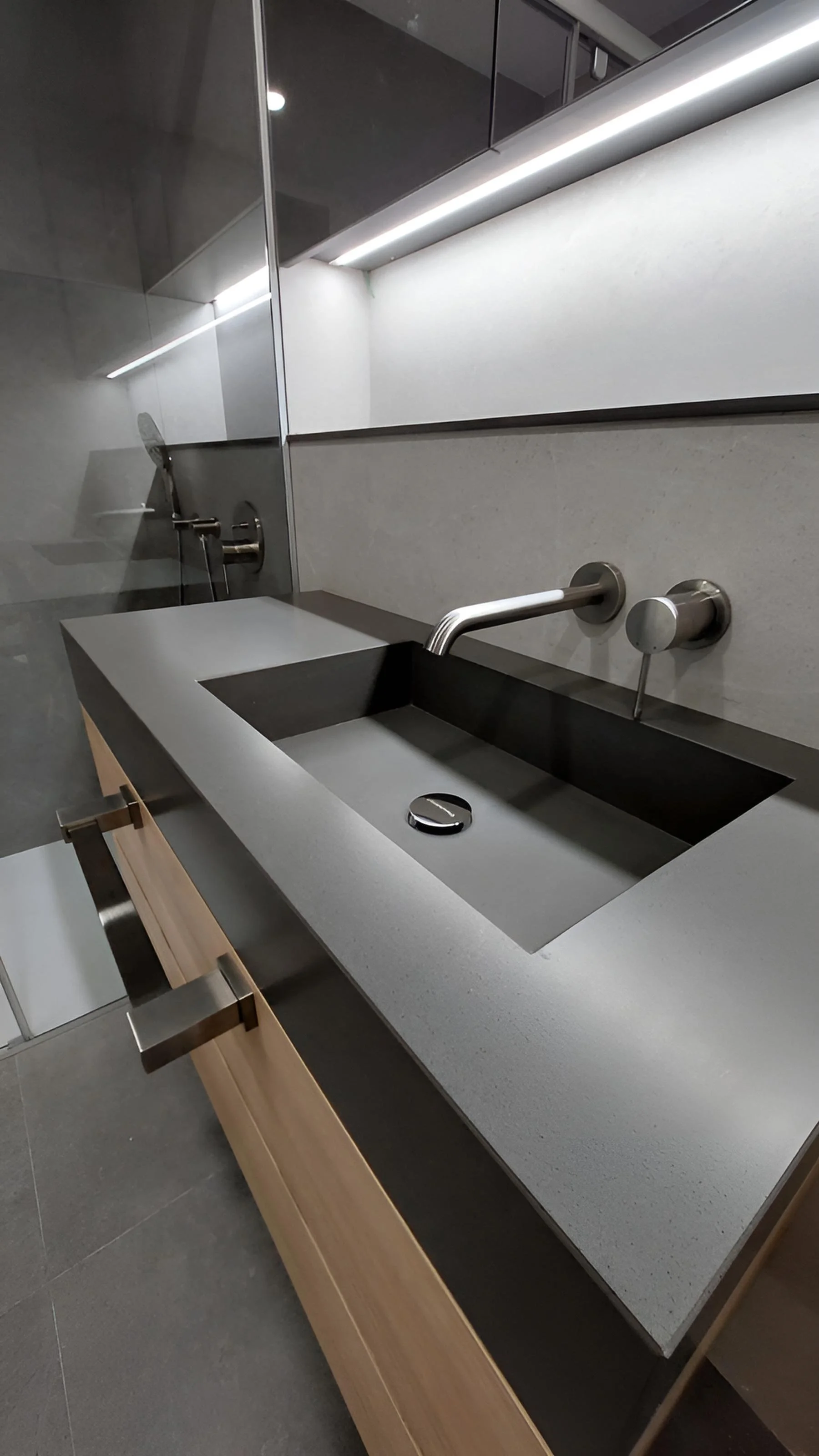 Lavabo moderno en una cocina con fregadero rectangular negro, encimera de piedra gris, grifo de metal y armario de madera debajo.