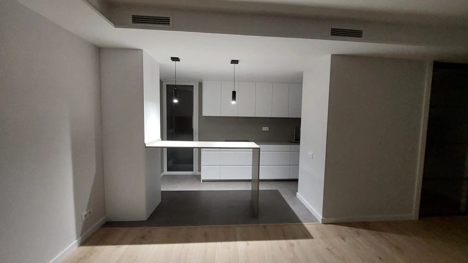 Cocina moderna con armarios blancos, encimera y ventana, luz suspendida, suelo de madera.