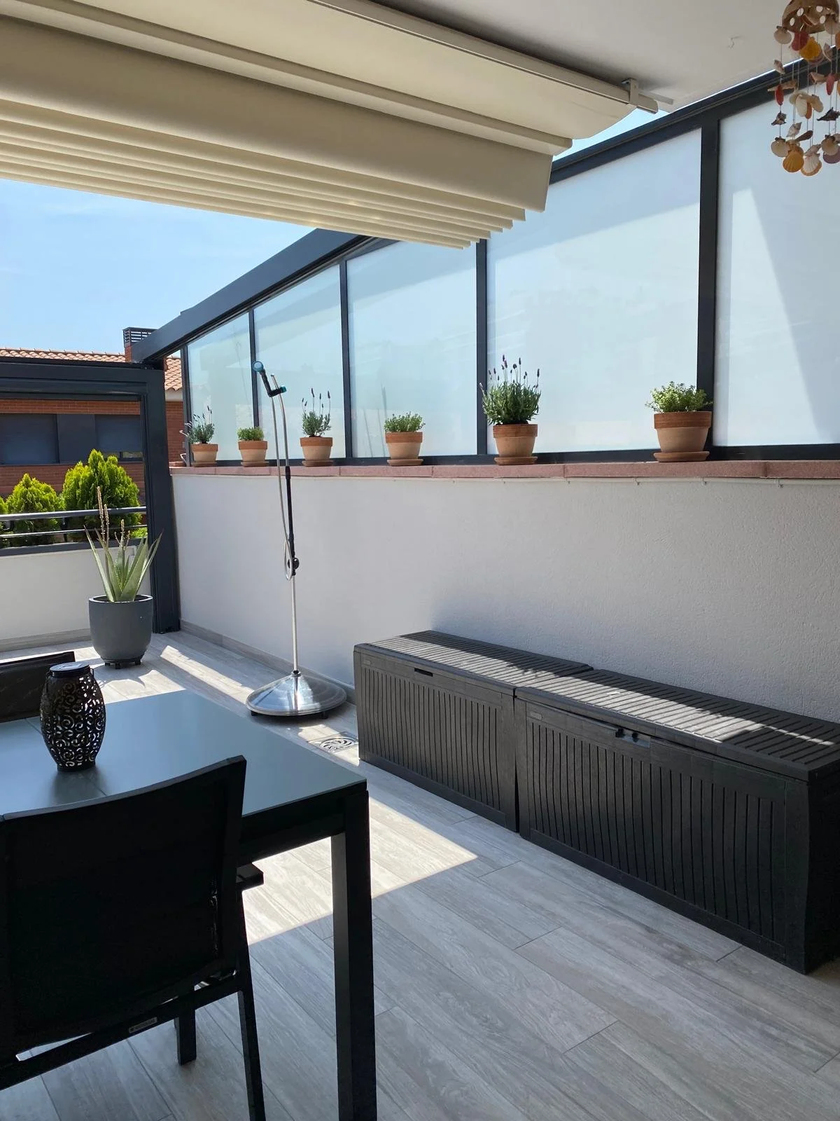 Balcón con plantas en macetas y mobiliario, piso de madera clara, vista del cielo y árboles.