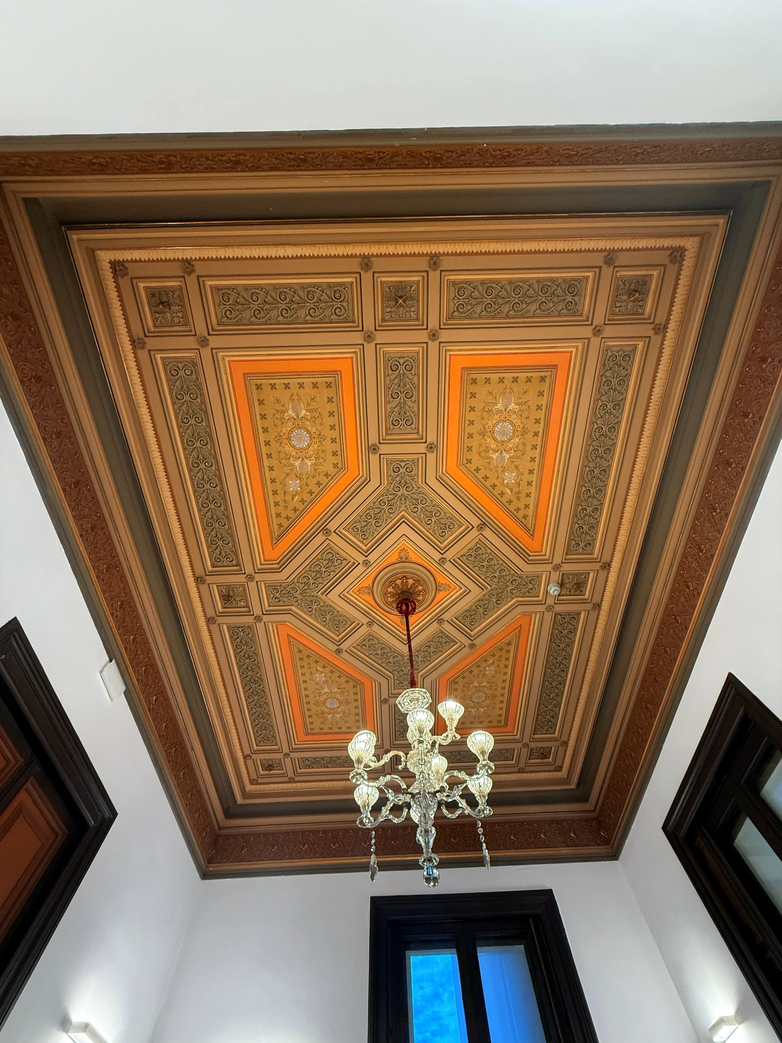 Techo decorado con molduras y un candelabro de cristal en una habitación con paredes blancas y ventanas con marcos oscuros