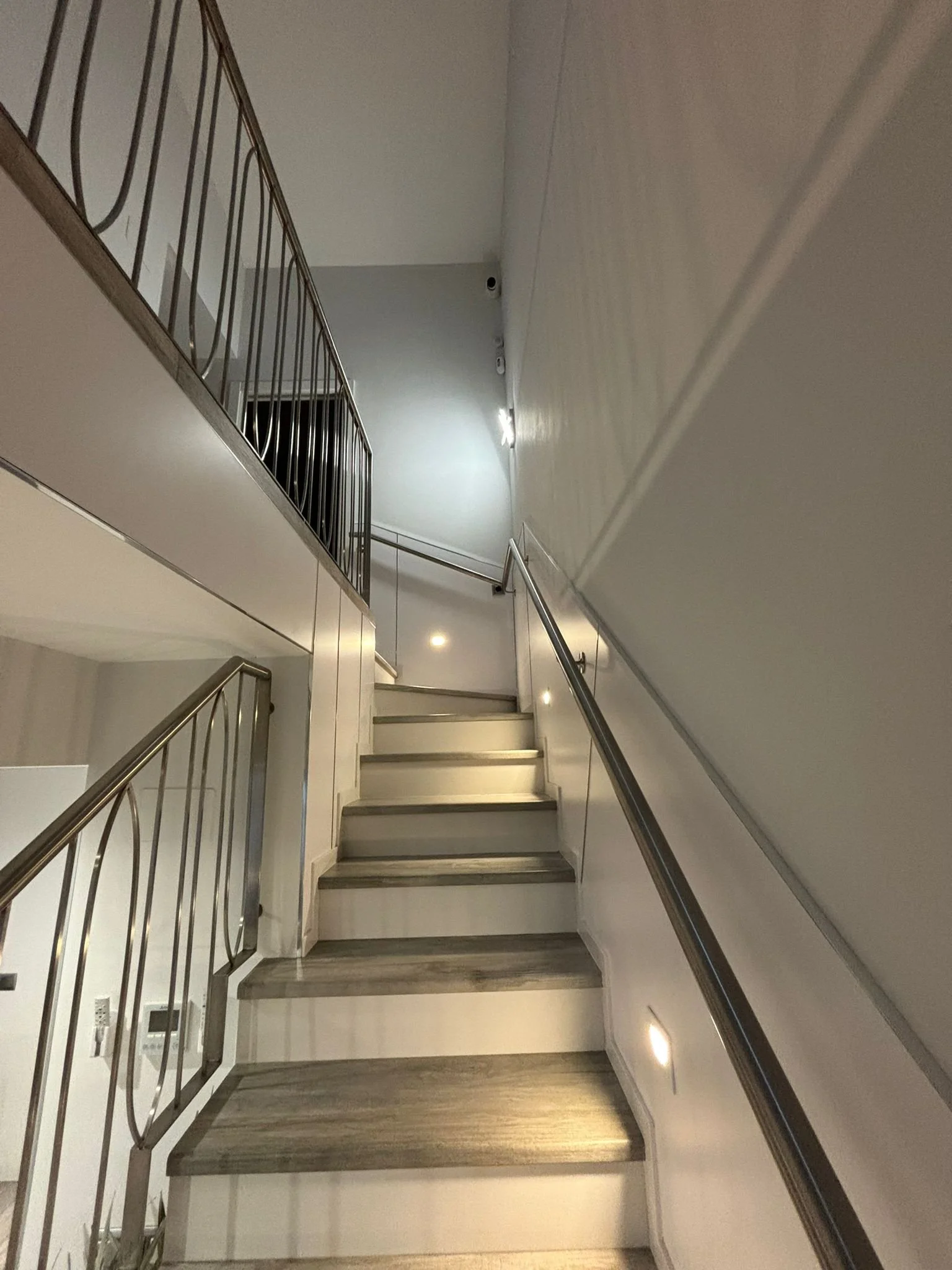 Escalera interior con pasamanos de metal, paredes blancas y iluminación empotrada en el techo.