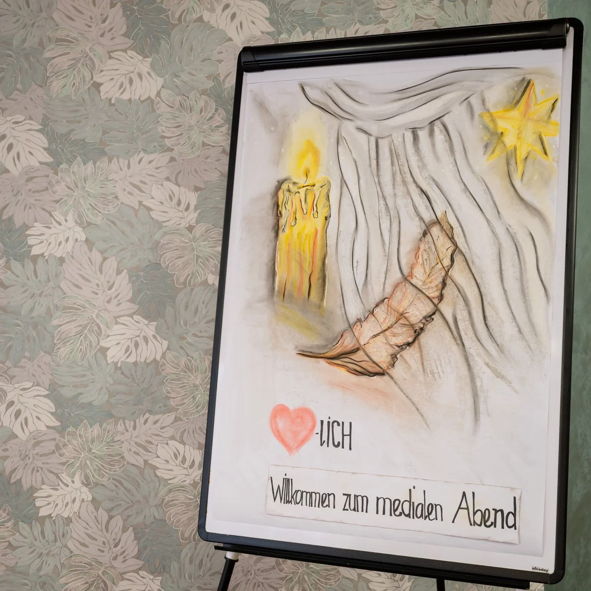 Einer handgezeichneten Illustration, die eine Kerze, einen Stern, eine Feder und einen Spruch enthält. Der Spruch lautet: 'Herzlich Willkommen zum medialen Abend'.