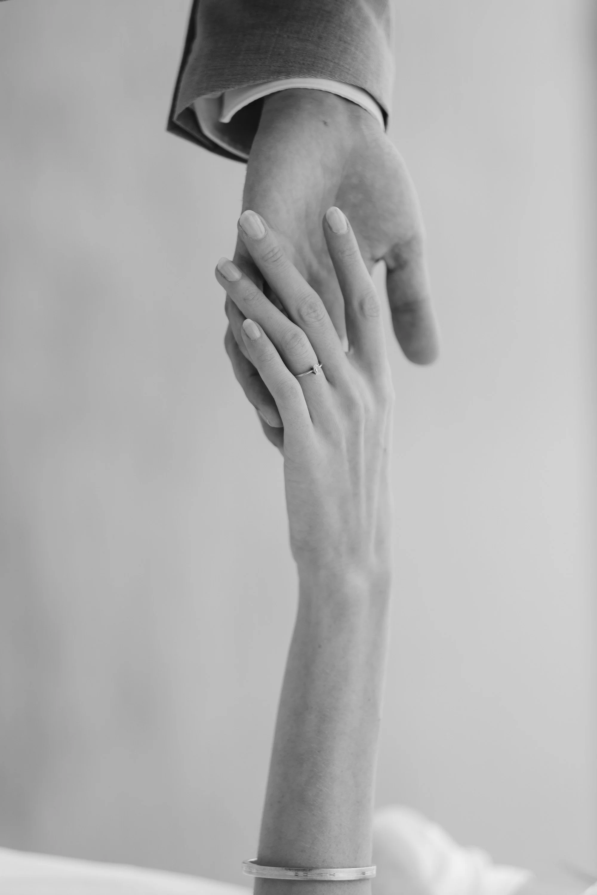 A hand, with a ring on the ring finger, gently holds another hand from above, with a blurred background.