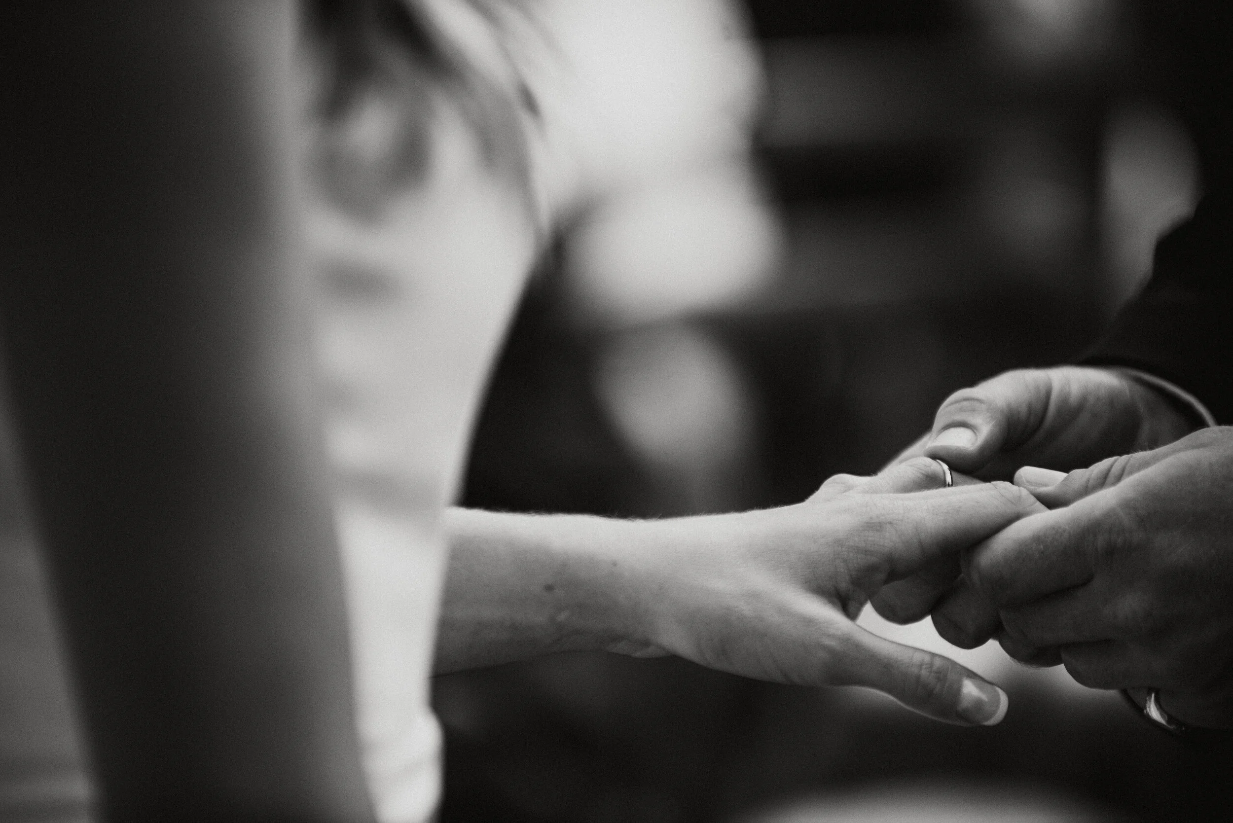 Close-up of a wedding ring being placed on a woman's finger during a wedding ceremony, in black and white.