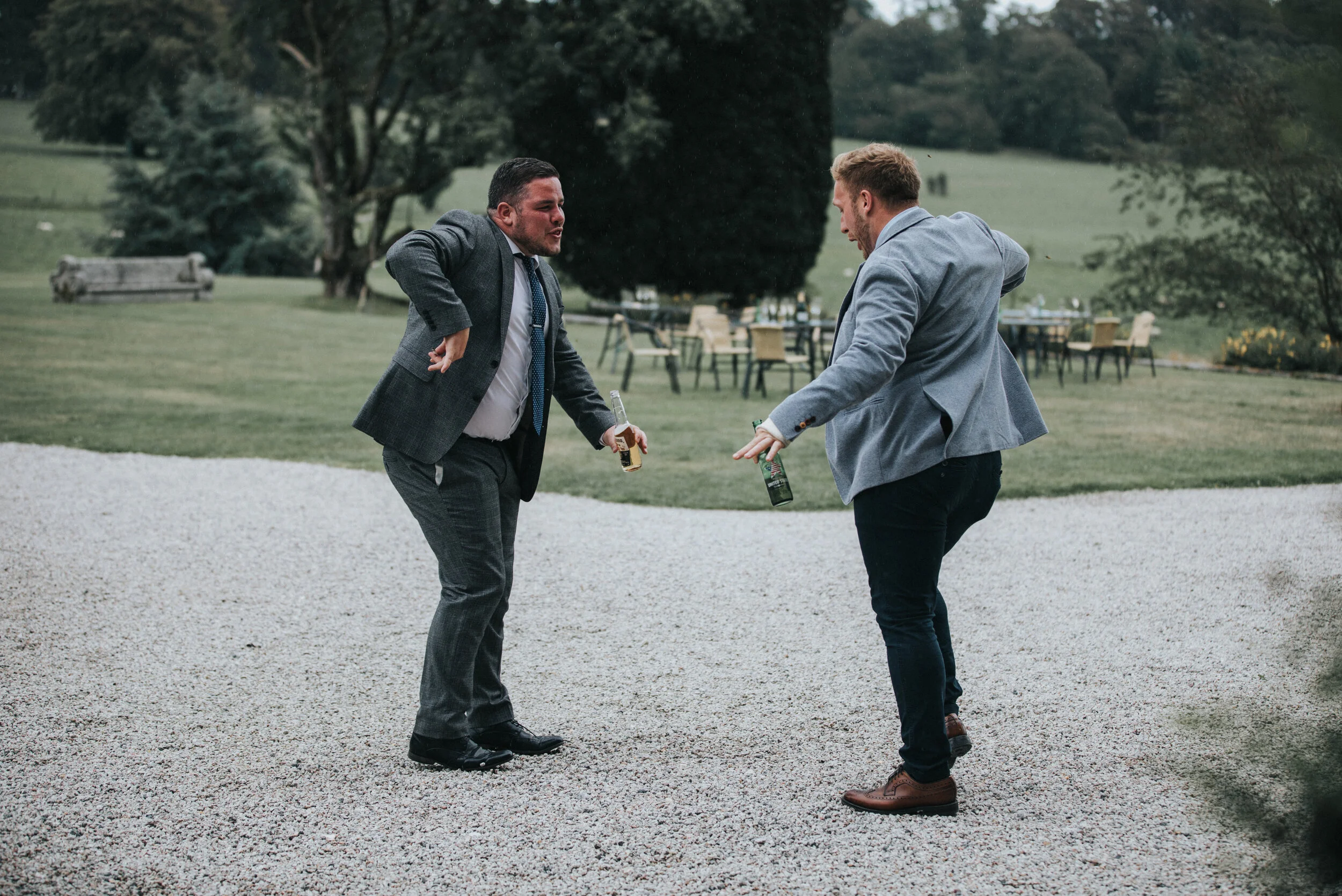 Two men in suits arguing and fighting each other outdoors with beer bottles in hand.