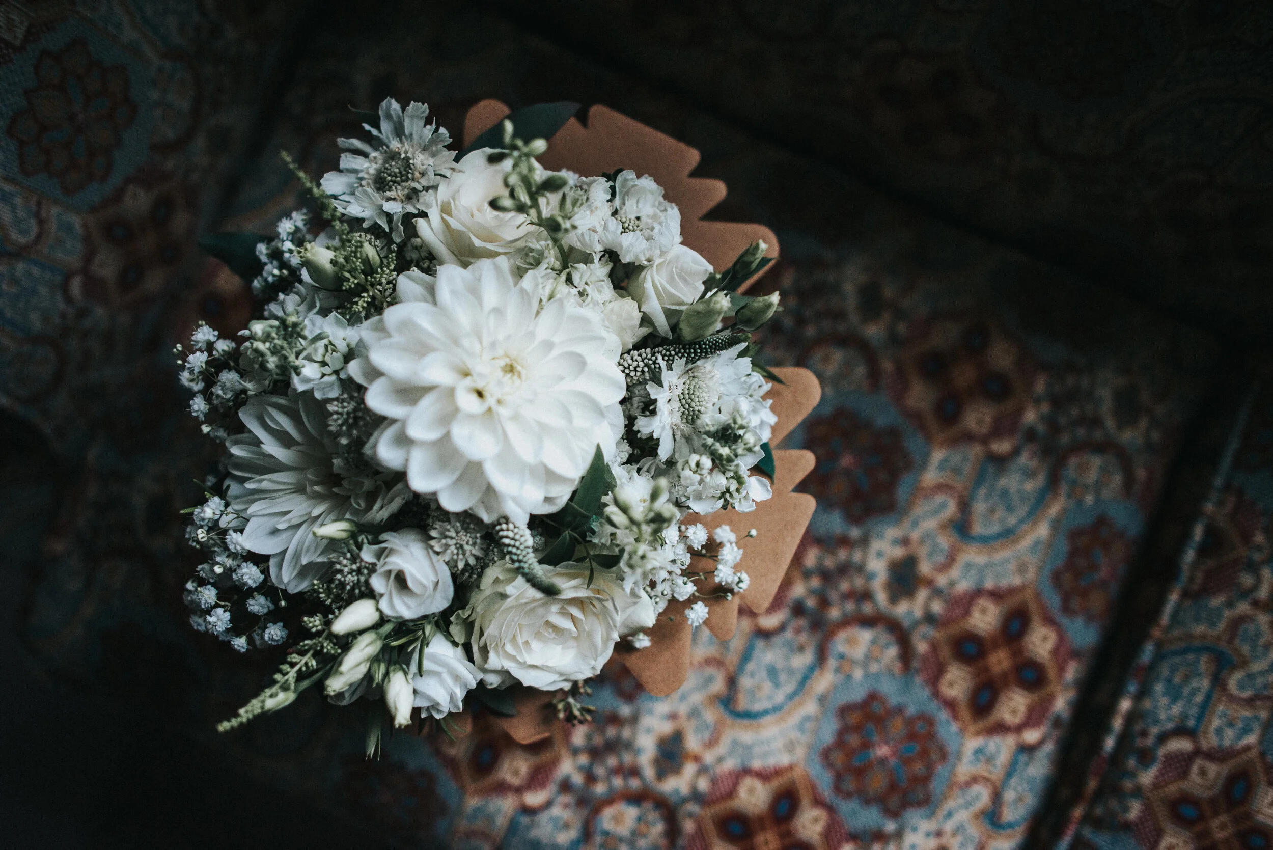 A bouquet of white flowers including roses and dahlias on a patterned rug.