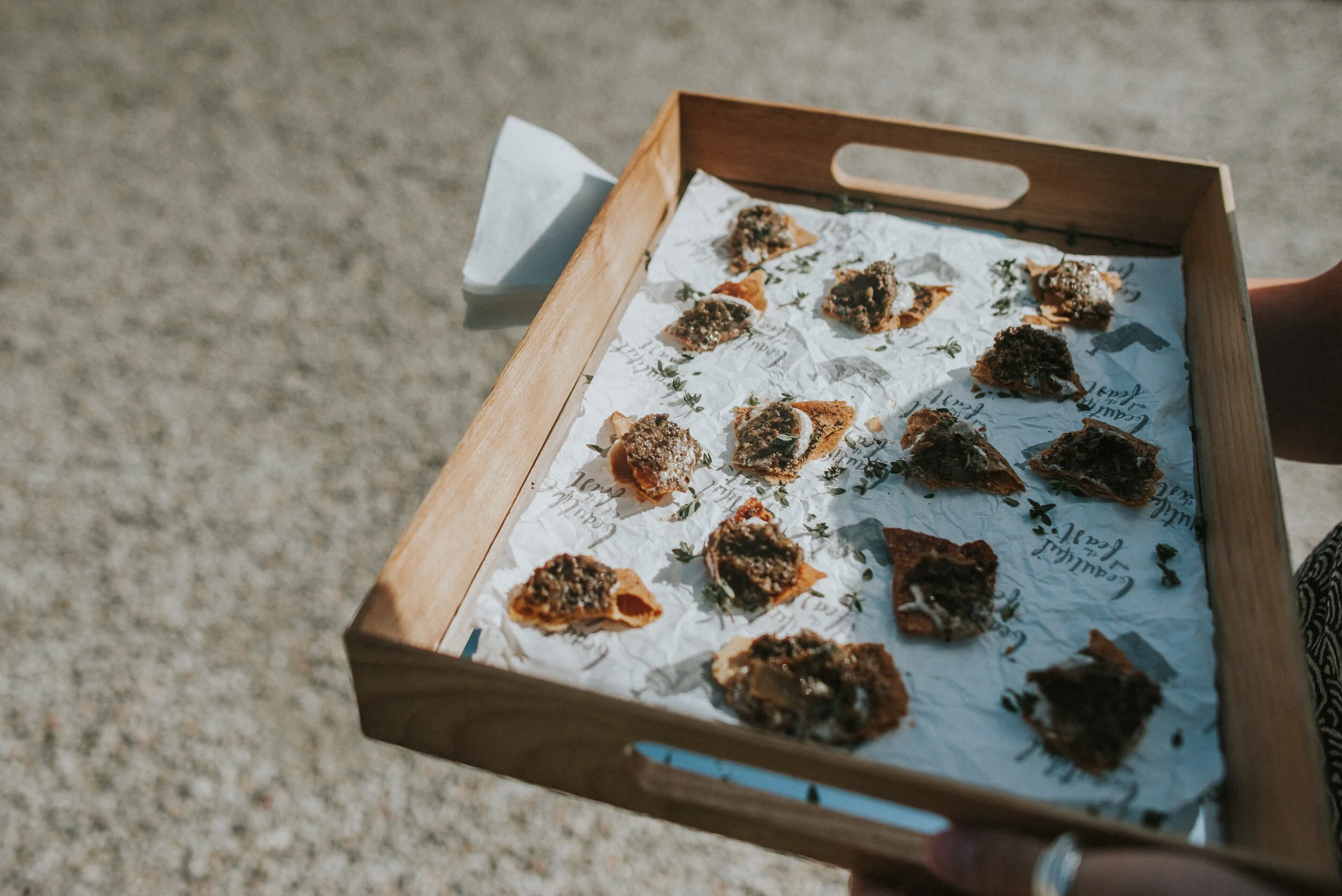 Tray of assorted small appetizers or snacks on parchment paper outside on a concrete surface.