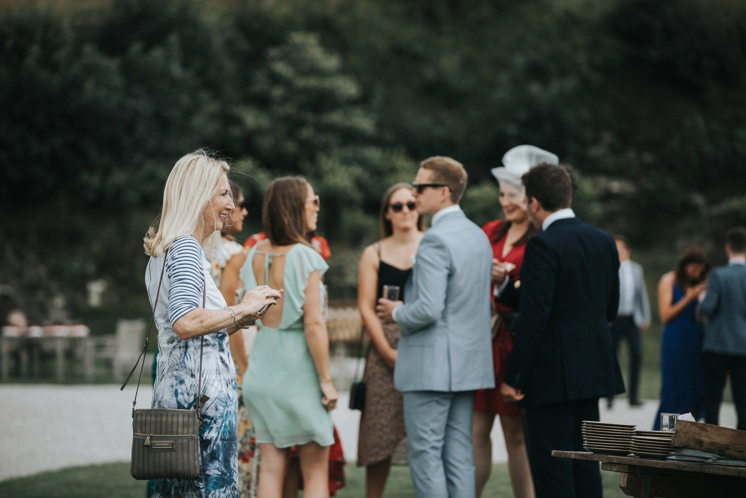 People socializing at an outdoor event by a lake, dressed in semi-formal attire.