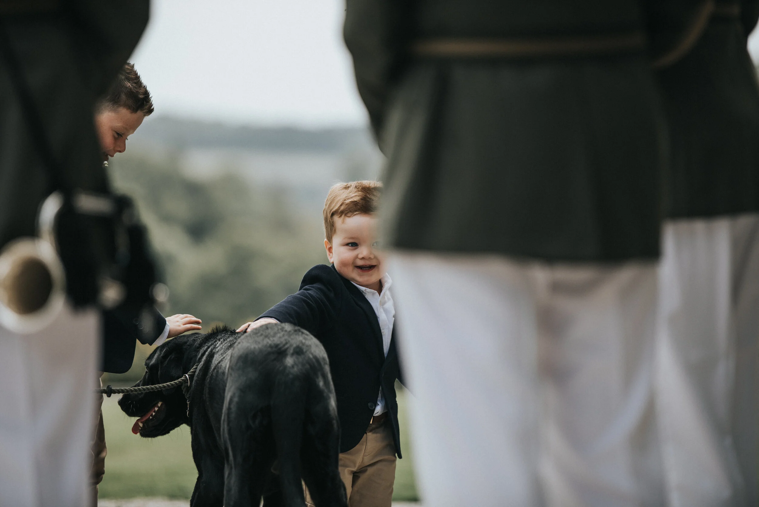 Young boy smiling and petting a black dog, surrounded by adults.