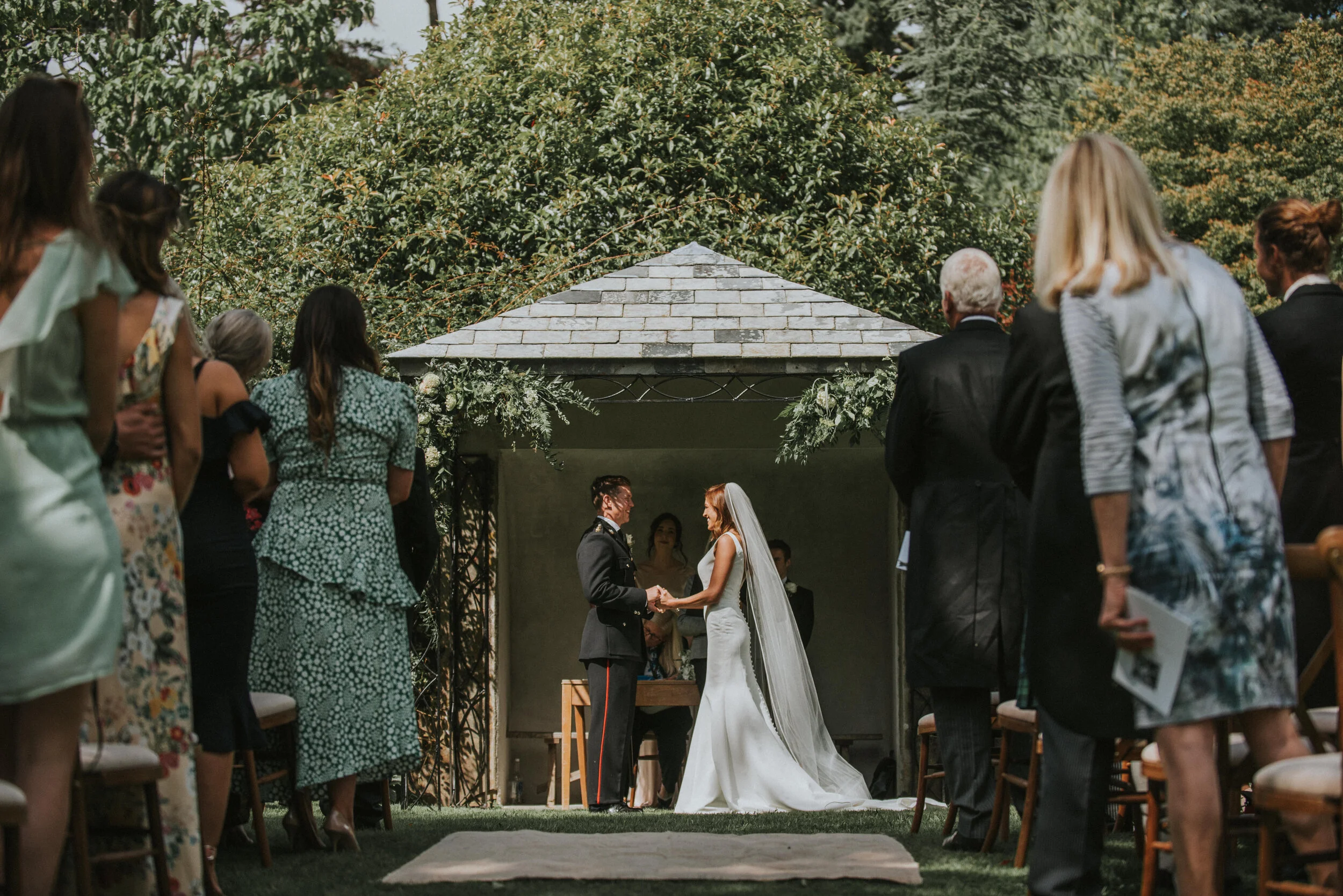 A wedding ceremony taking place outdoors with a bride and groom holding hands and exchanging vows.