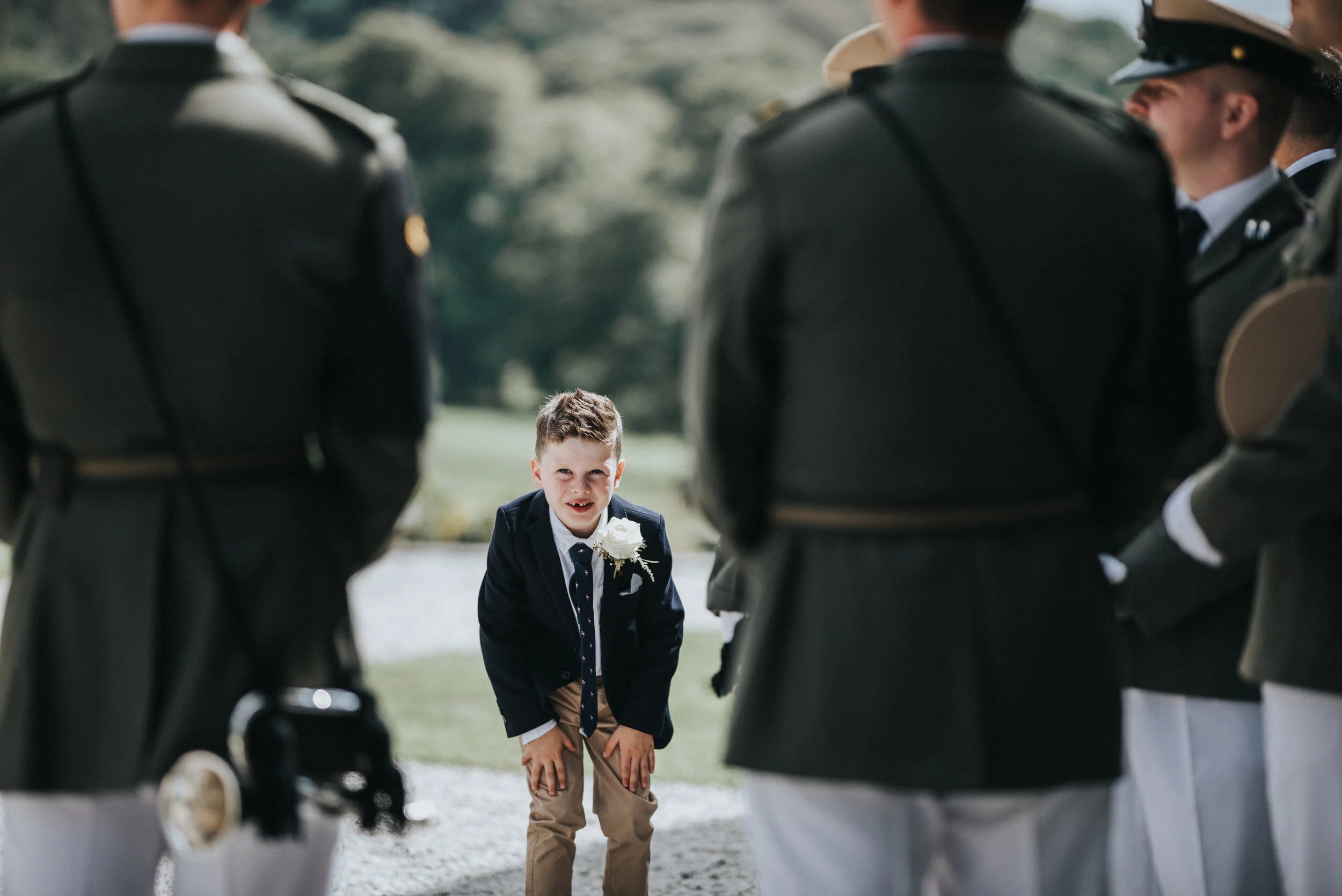 Young boy dressed in a suit is bowing to soldiers in uniform during an outdoor ceremony.