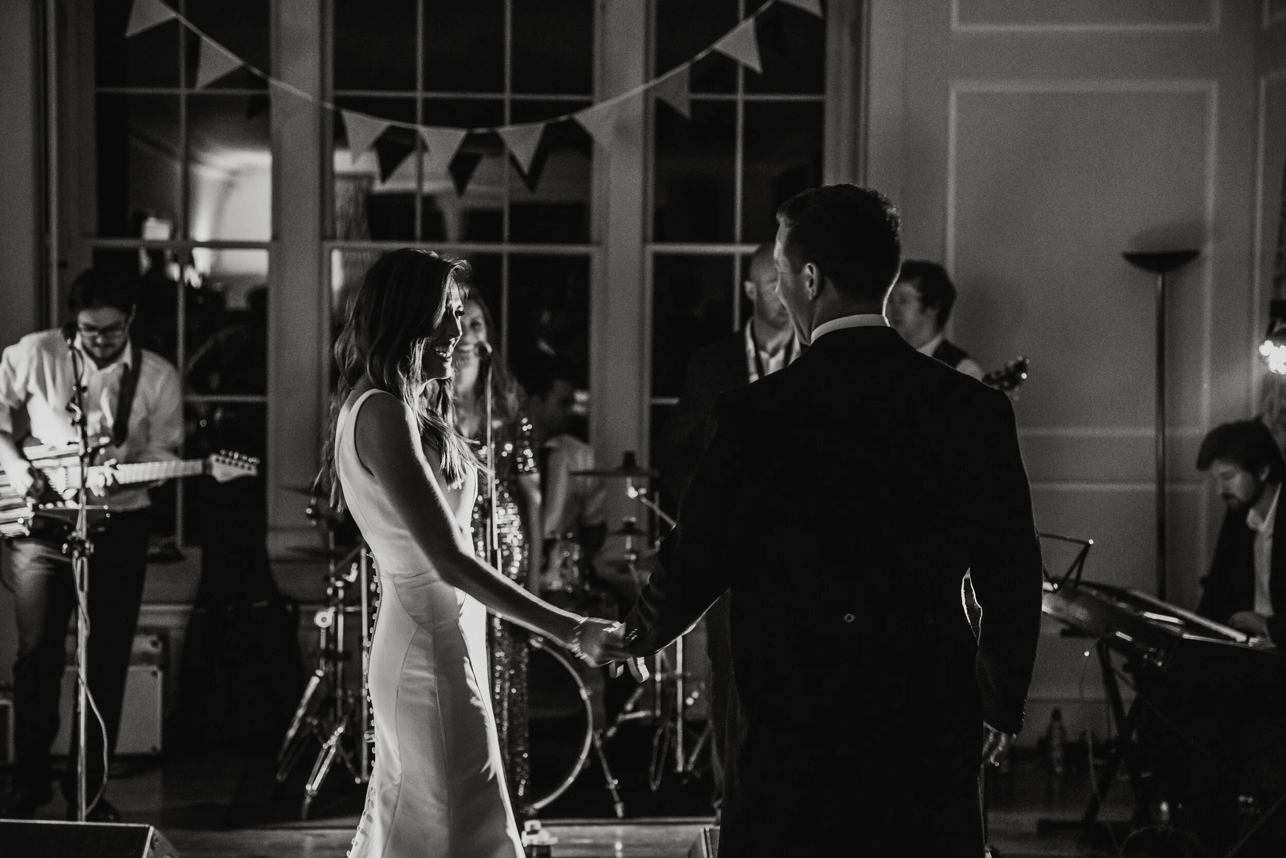 A black-and-white photo of a couple dancing at their wedding reception with a band playing in the background.