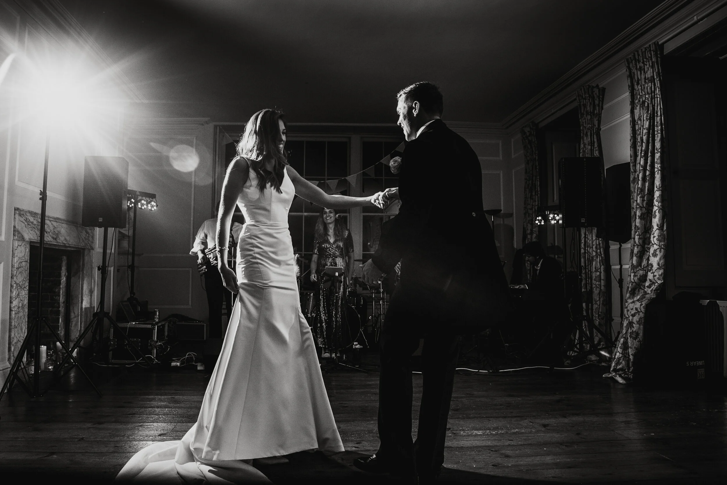 A bride and groom dancing at their wedding reception in a decorated ballroom with a live band playing in the background.