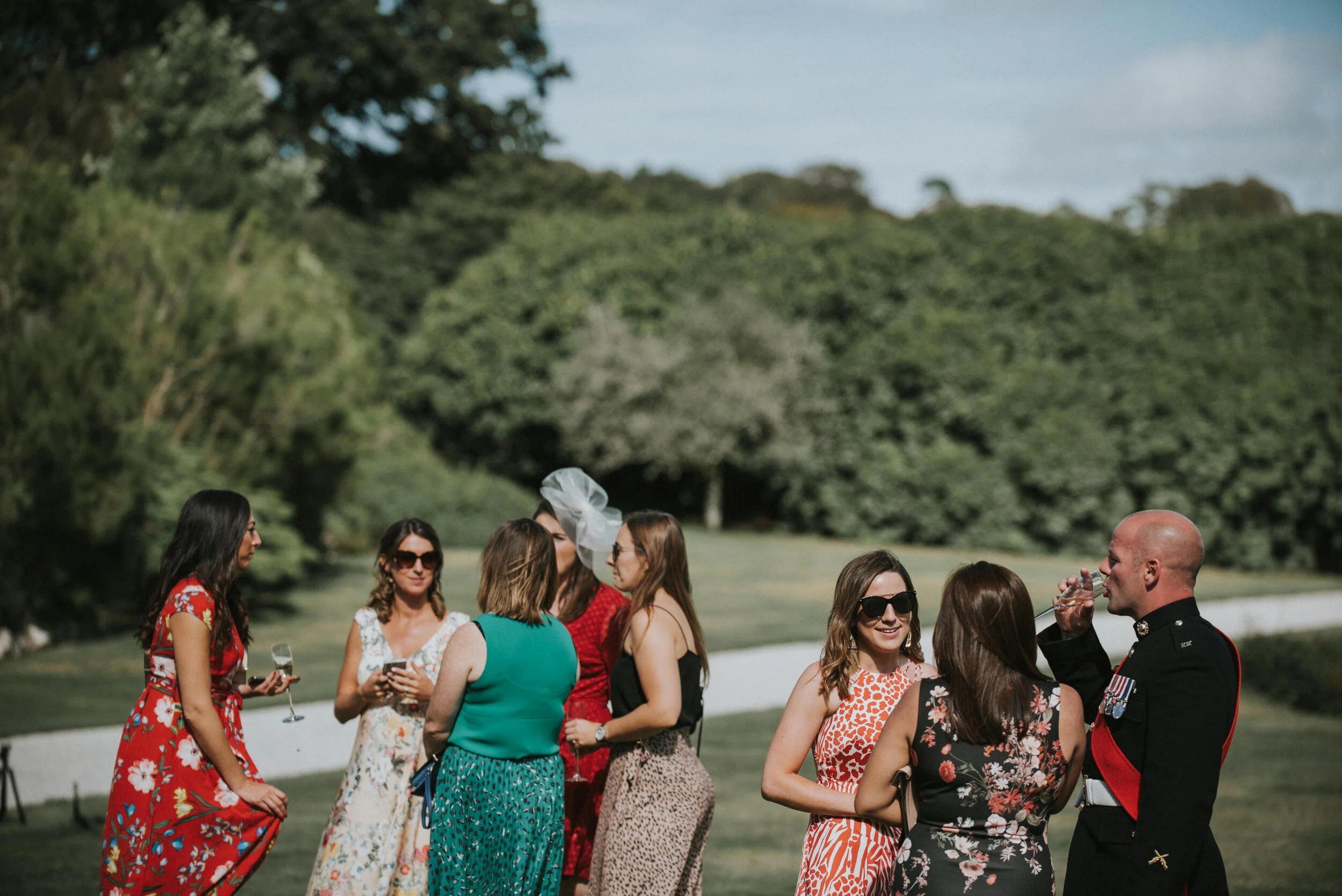 Group of women in dresses and a man in military uniform at outdoor social gathering on a sunny day