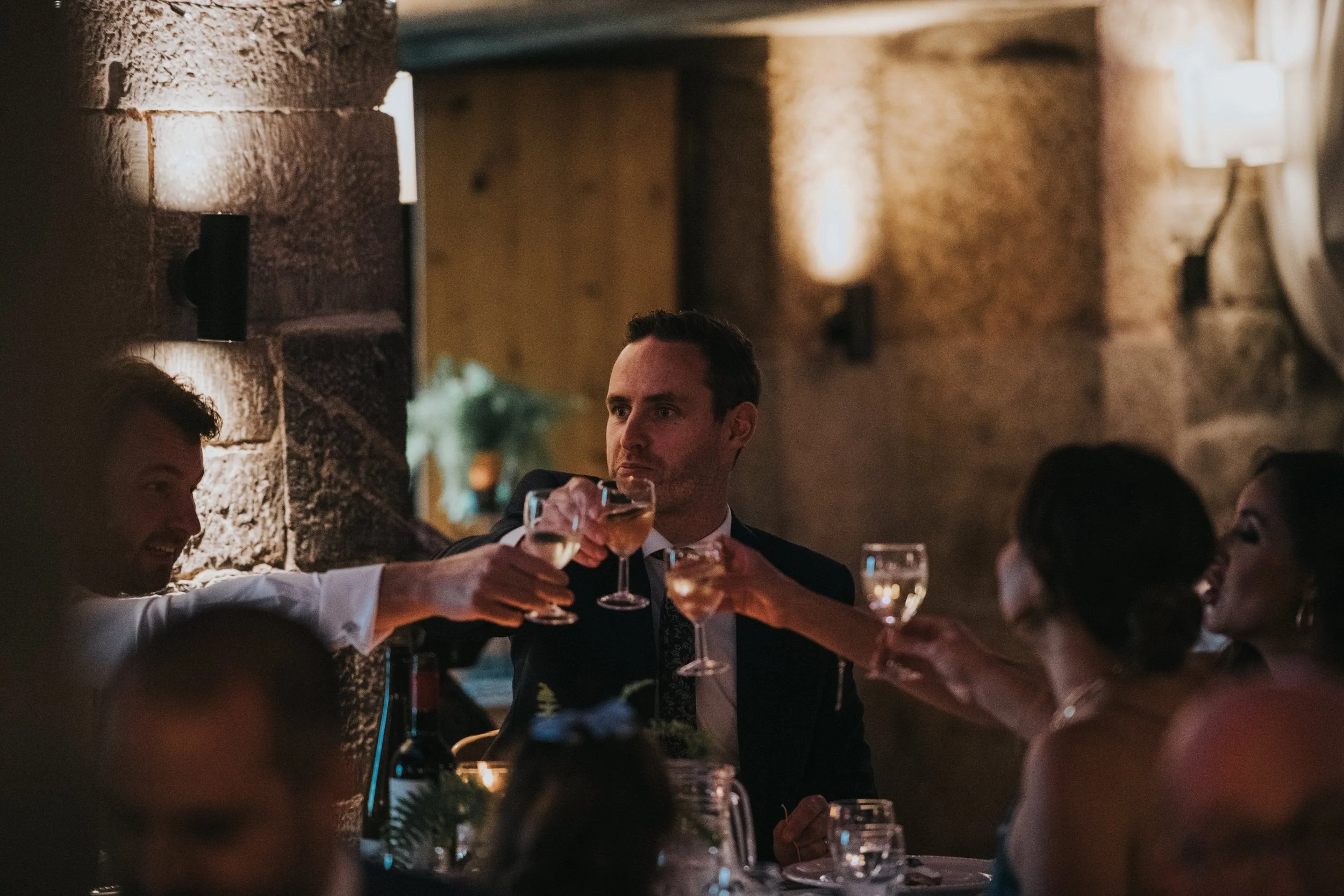 People at a dinner party raising glasses for a toast in a warmly lit, rustic restaurant.