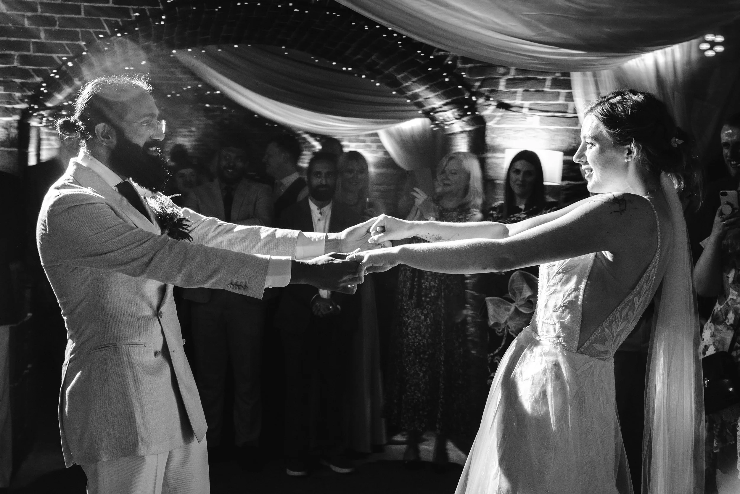 A bride and groom dancing at their wedding reception, with guests watching in an intimate, decorated venue.