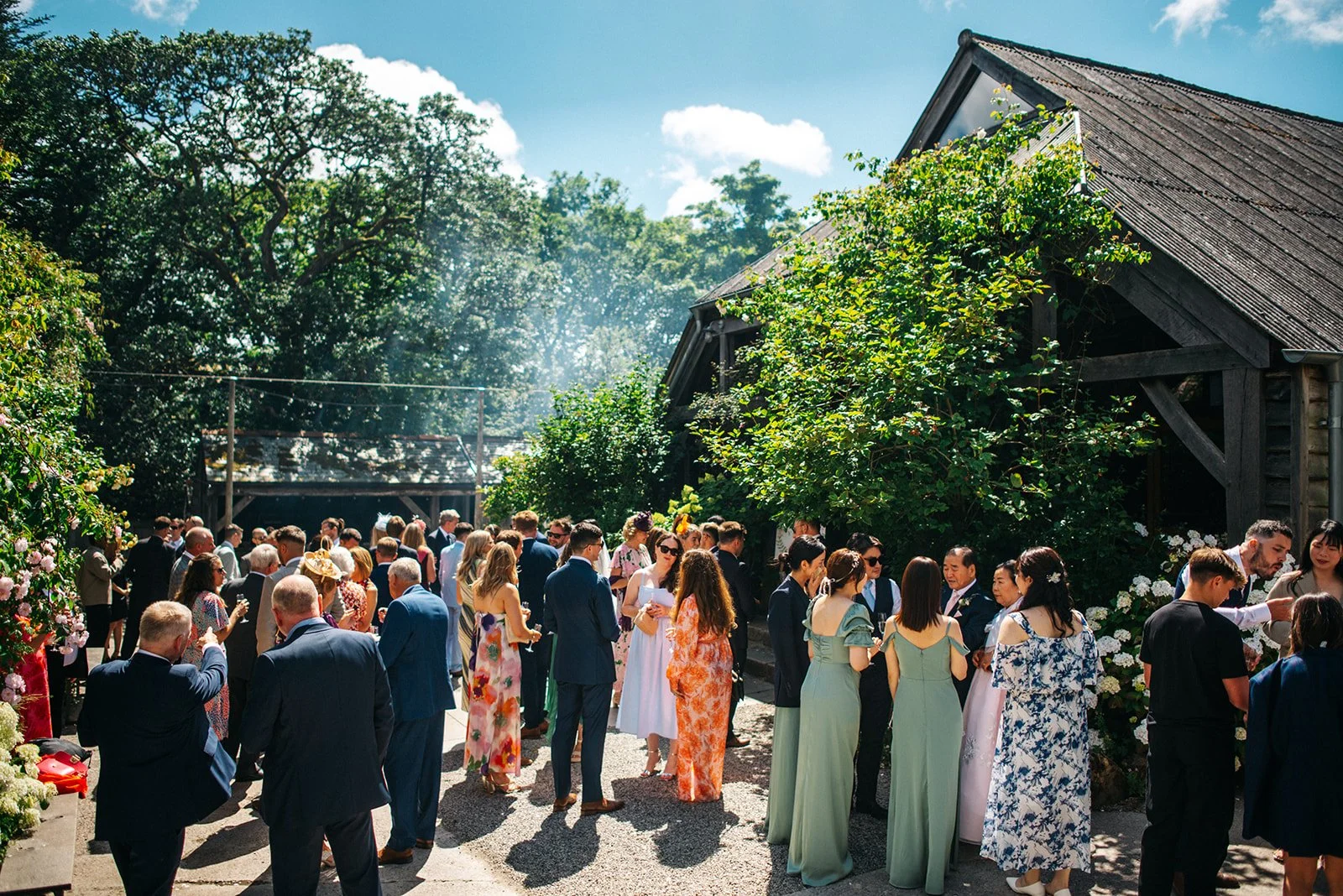 People dressed in formal attire gathered outdoors near a rustic wooden building with trees in the background.