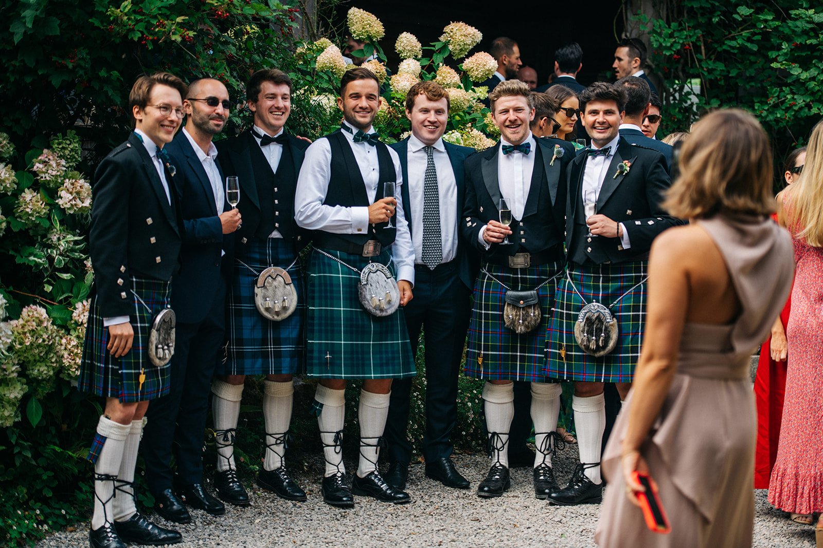 A group of men dressed in traditional Scottish attire, including kilts, jackets, and sporrans, standing together and smiling at a social event or celebration.