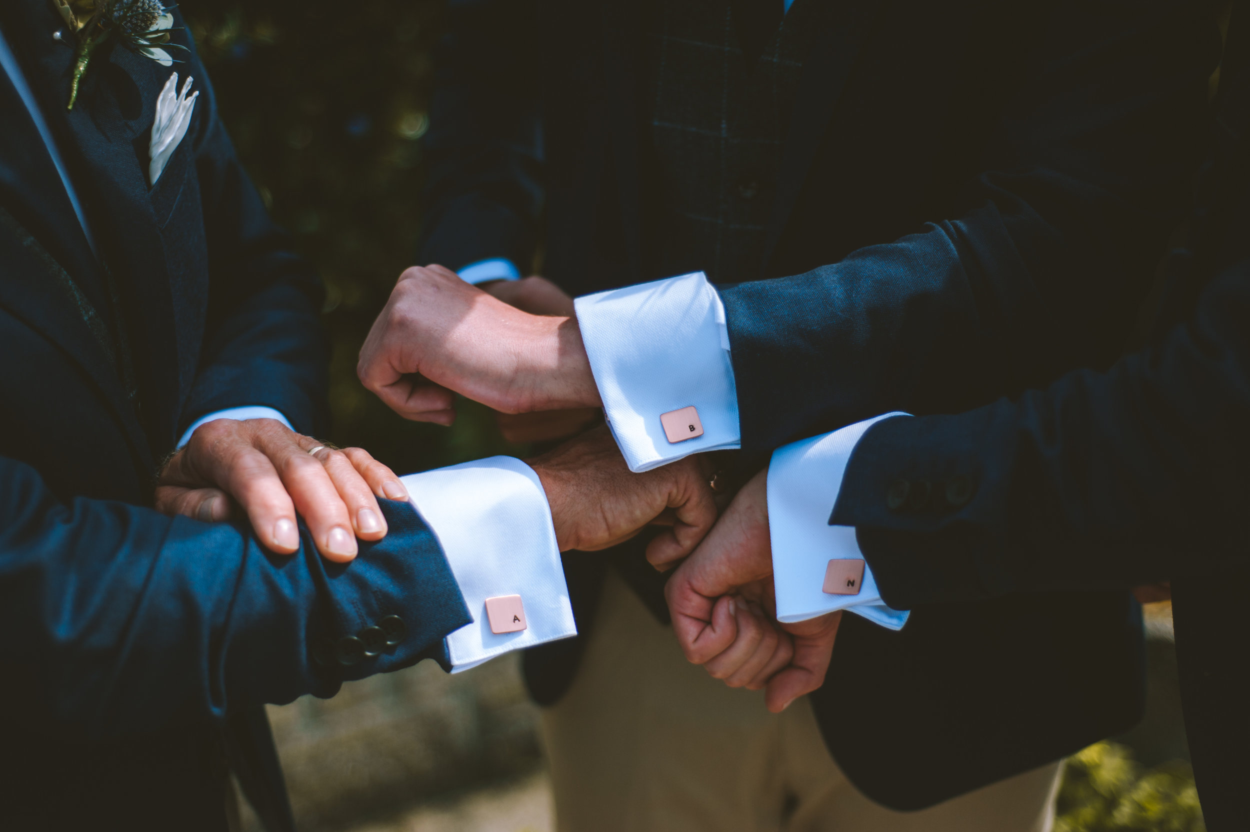 Two men in suits exchanging rings during a wedding ceremony, with each man's hand wearing a cufflink labeled 'A' and 'B'.