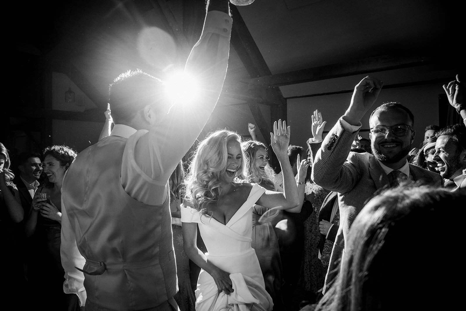 People dancing and smiling at a celebration, with one woman in a white dress and others raising their arms in joy.