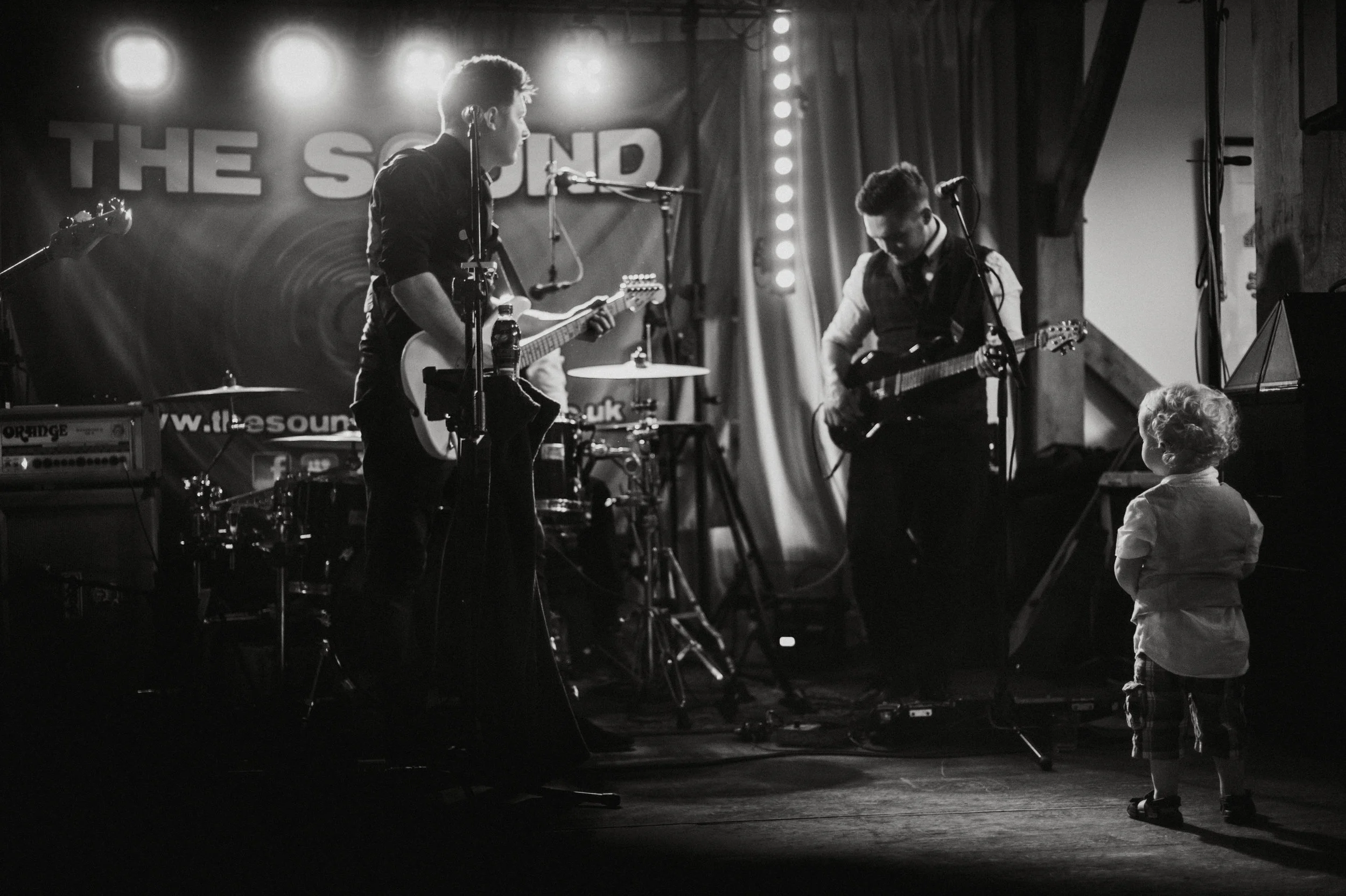 A young child stands in front of a live band playing on stage, captivated by the performance.