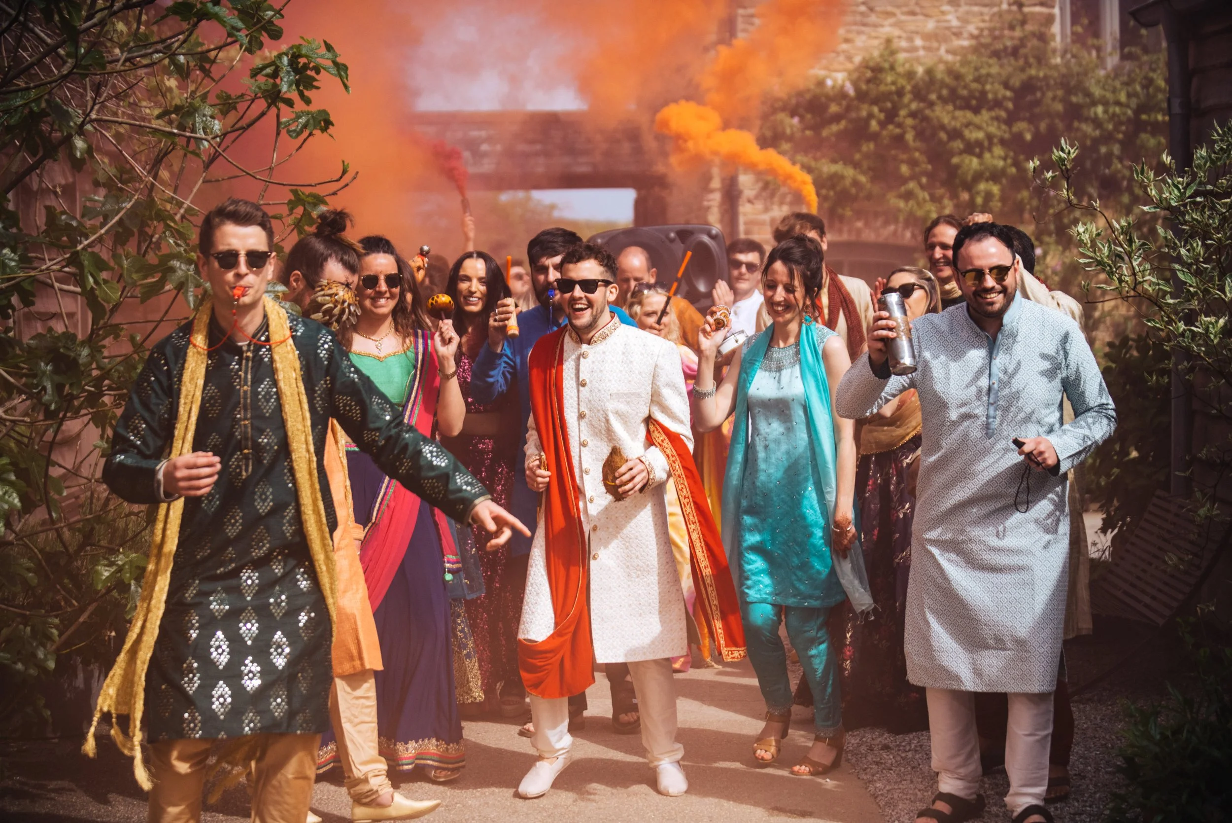 People celebrating and dancing outdoors during a colorful festival with smoke and powder explosions in the air, dressed in traditional and festival attire.