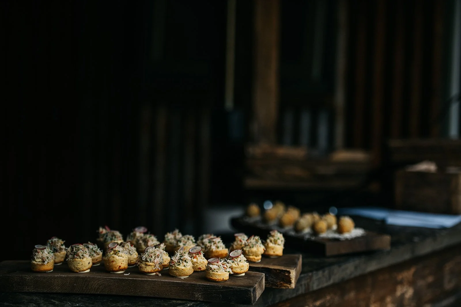 Assorted canapés with toppings on wooden boards in a rustic setting.