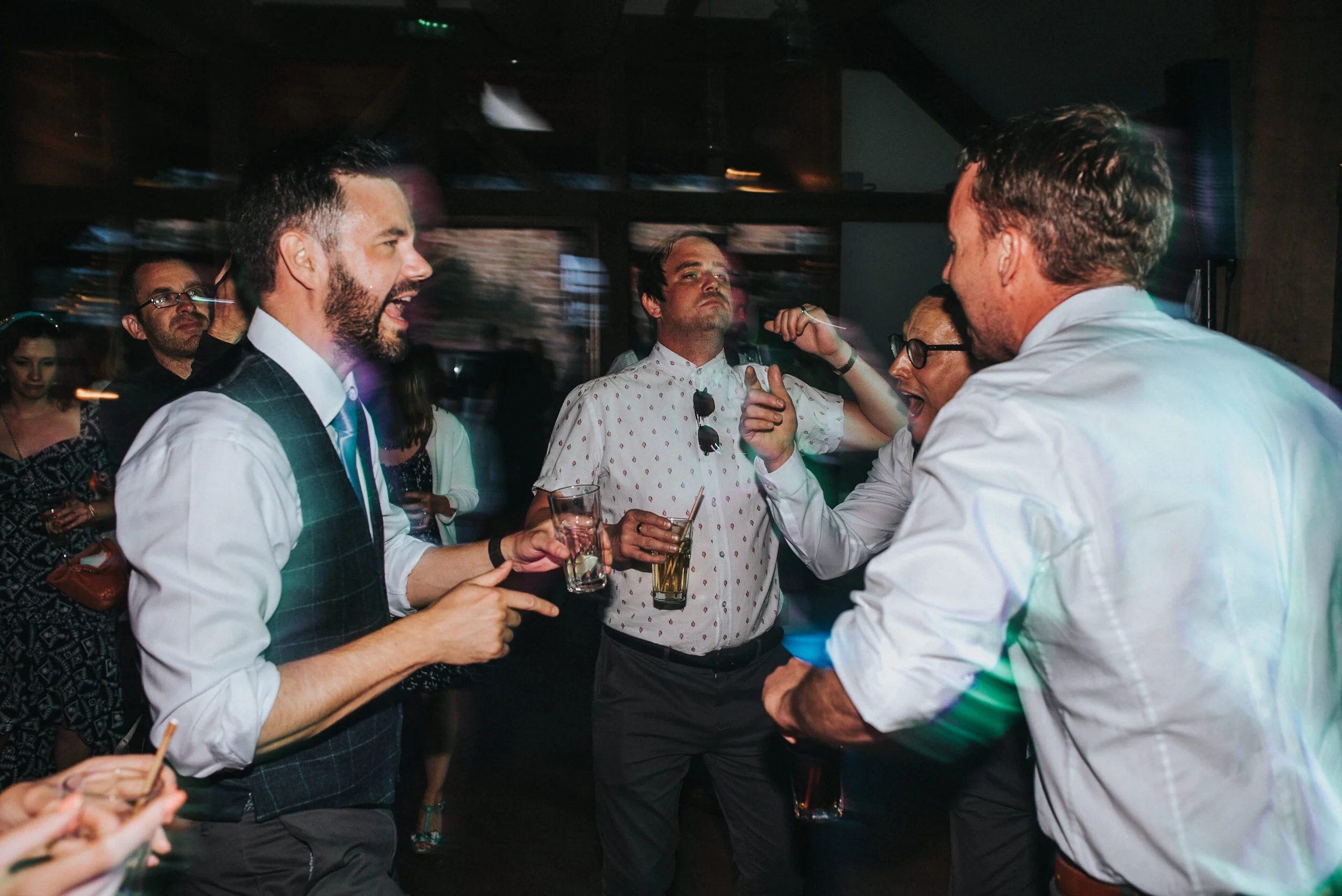 Group of people dancing and socializing at a party or bar, with some holding drinks, in a lively indoor setting.