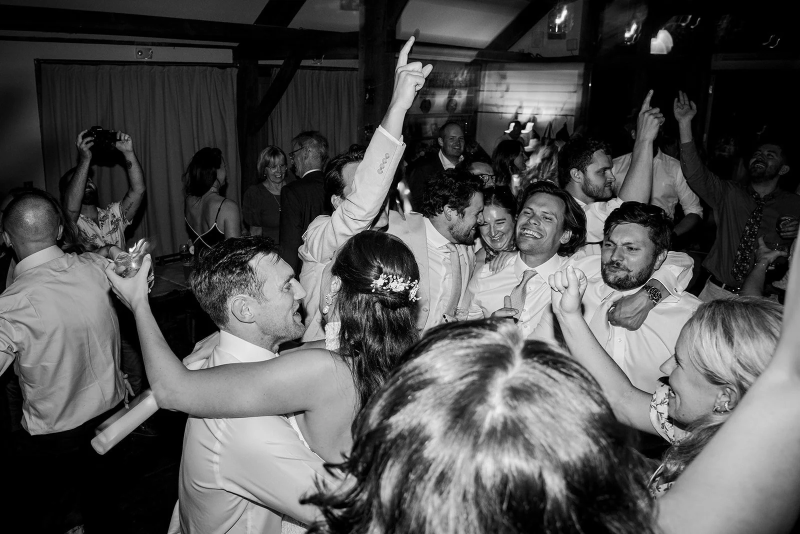 People dancing and celebrating at a lively social event, with smiles and raised hands, in a decorated indoor venue.