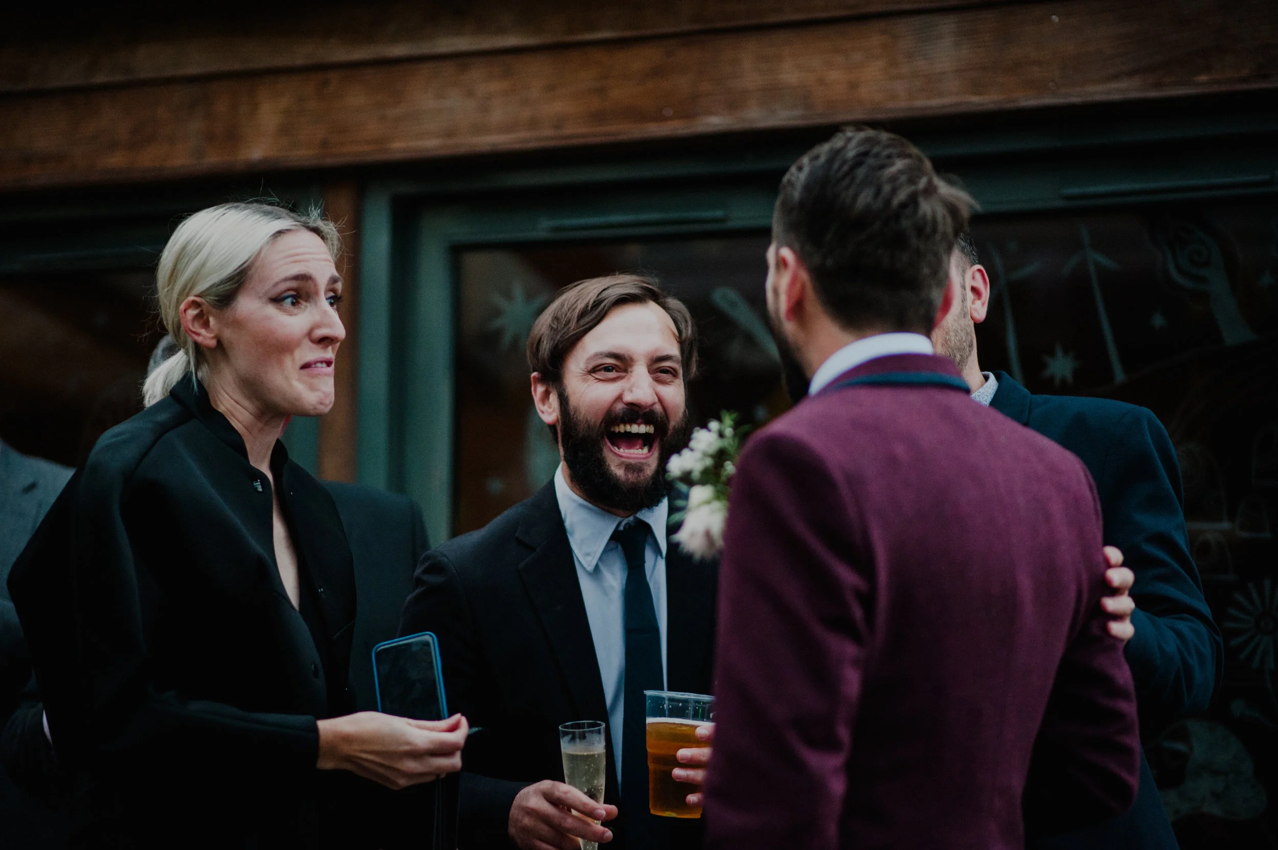 Group of people at a social gathering talking and laughing, with drinks in hand.