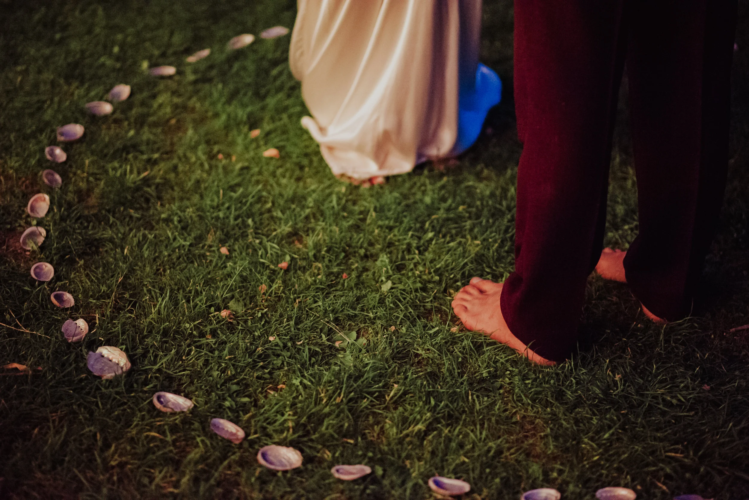 Footwear and clothing of two people standing on grass, with shoe shells arranged in a line on the ground.