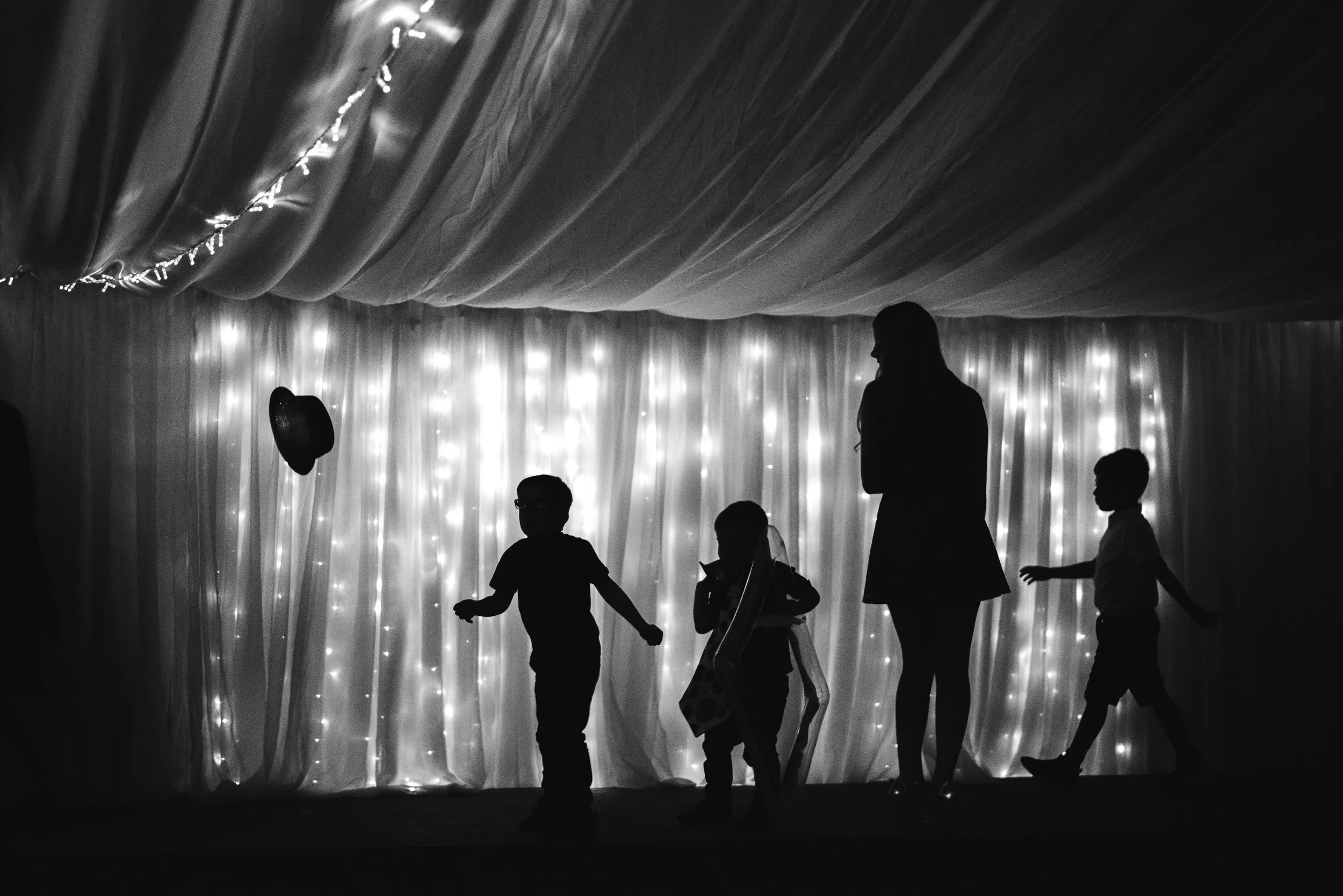 Silhouette of children and a woman standing on a decorated stage with twinkling lights and curtains in the background.