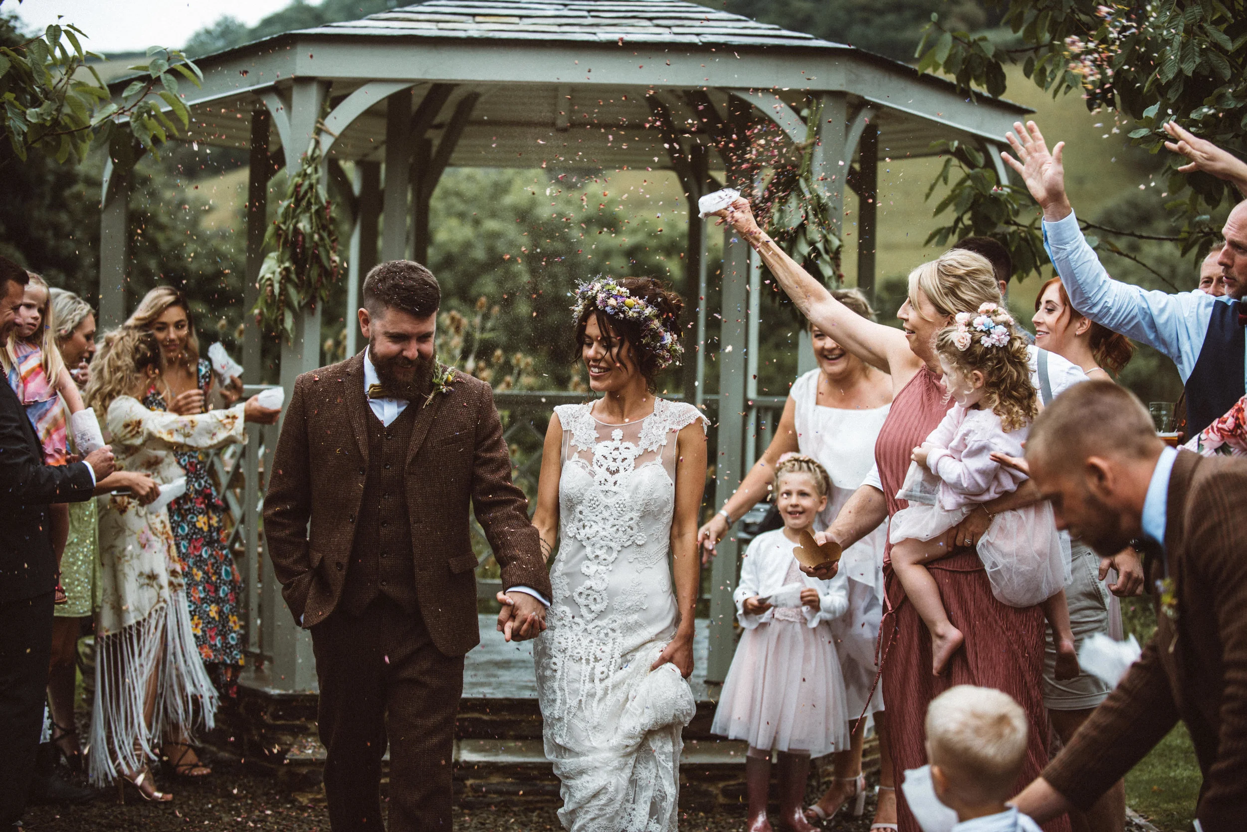Bride and groom holding hands walking through guests throwing confetti at outdoor wedding ceremony.