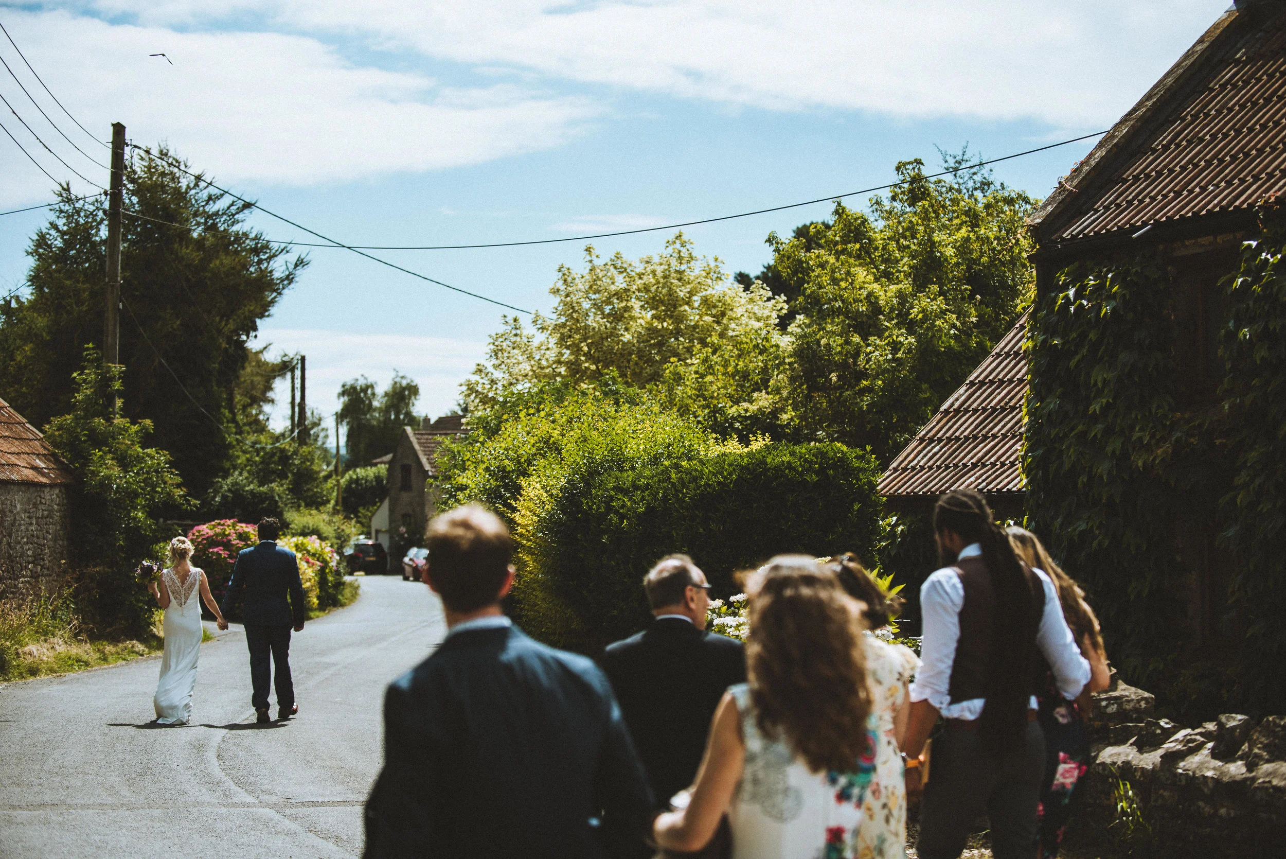Wedding captured by Cornwall wedding photographer Mark Shaw Photography - A wedding procession walking down a rural road in Cornwall