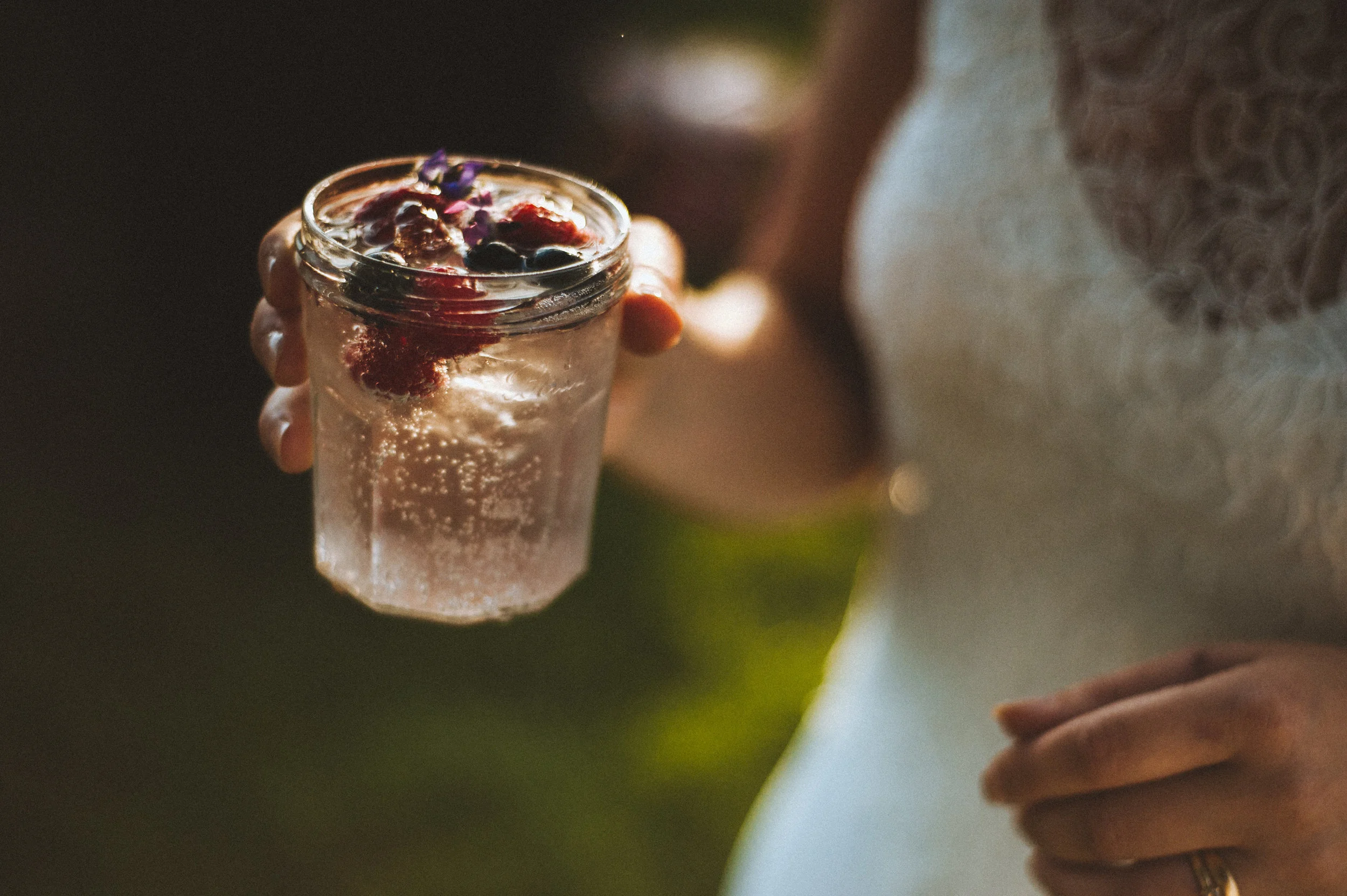 Wedding captured by Cornwall wedding photographer Mark Shaw Photography - Person holding a glass jar filled with clear sparkling water and topped with mixed berries and edible flowers.