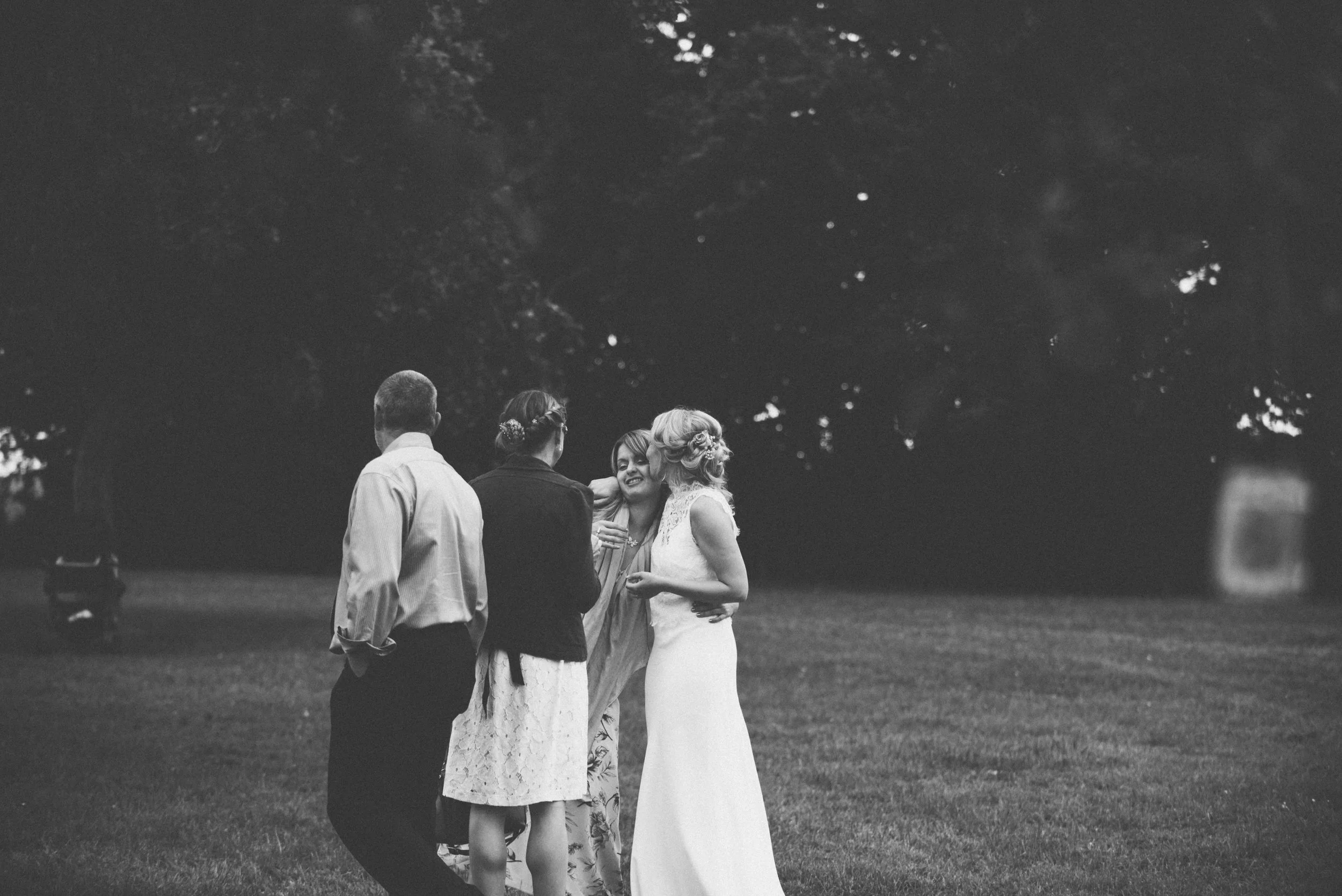 Wedding captured by Cornwall wedding photographer Mark Shaw Photography - Black and white photo of five people hugging outdoors, likely at a wedding, with trees in the background.