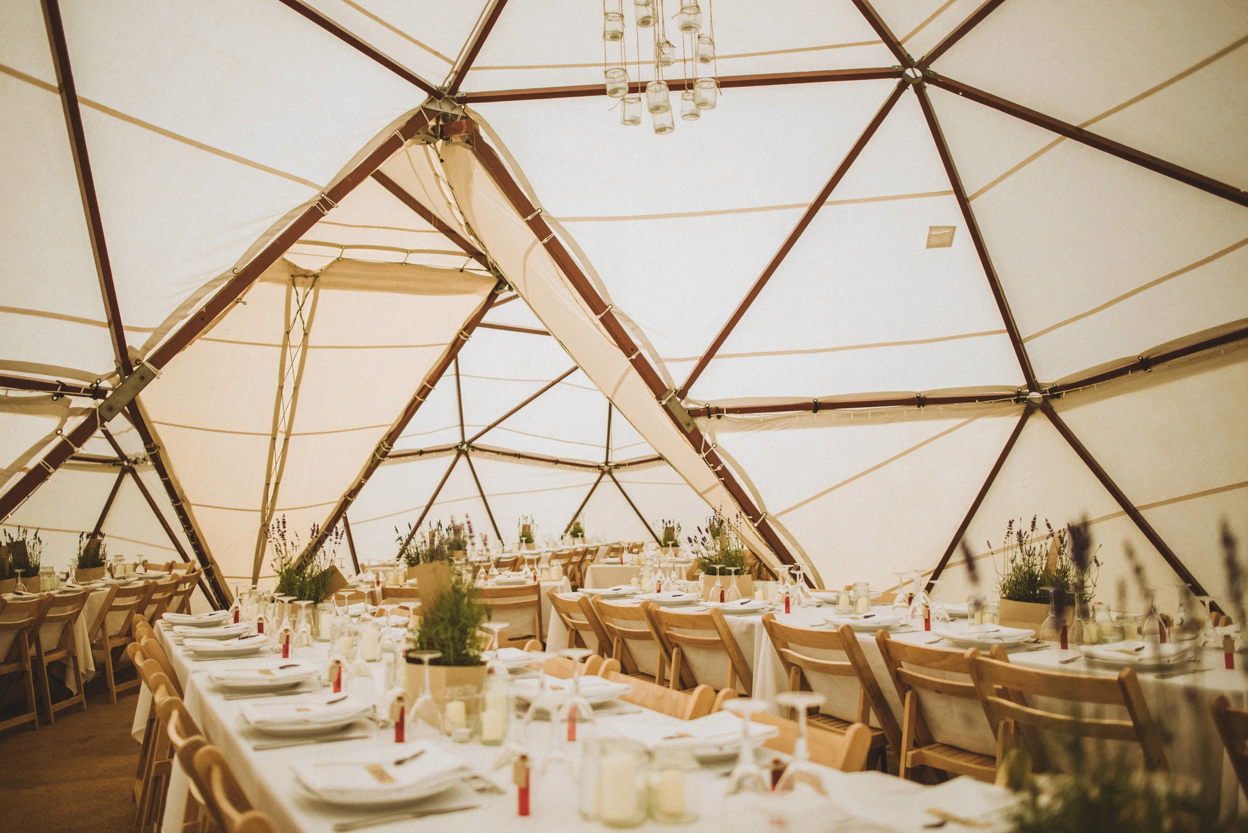 Pengenna manor wedding photography captured by Cornwall wedding photographer Mark Shaw Photography -Interior of a large event tent with arranged dining tables, white tablecloths, and wooden chairs, illuminated by hanging lights.