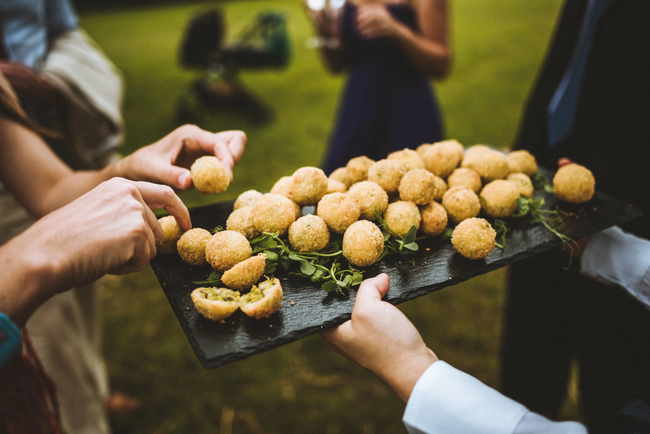 Wedding captured by Cornwall wedding photographer Mark Shaw Photography - People serving a platter of breaded, fried appetizers at an outdoor event.