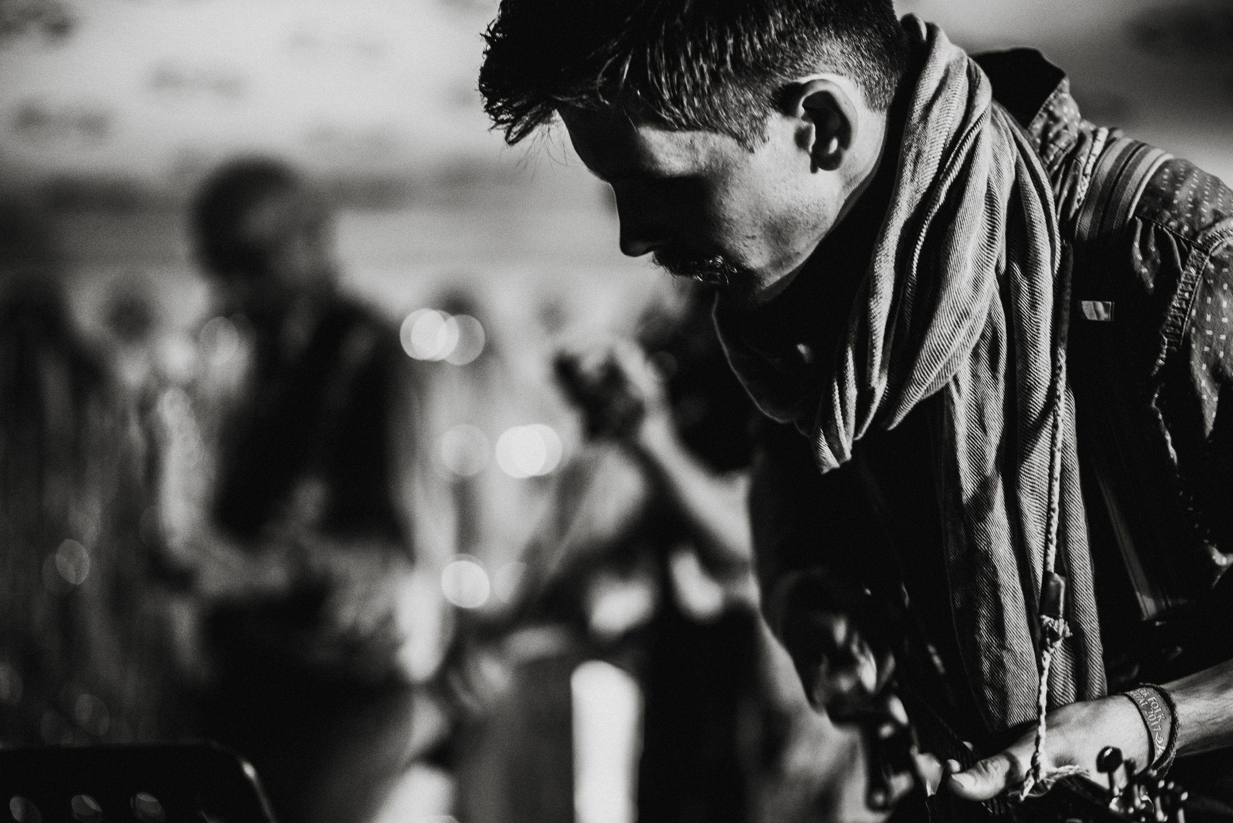 Black and white photo of a man with a scarf around his neck leaning forward, with several blurred people in the background.
