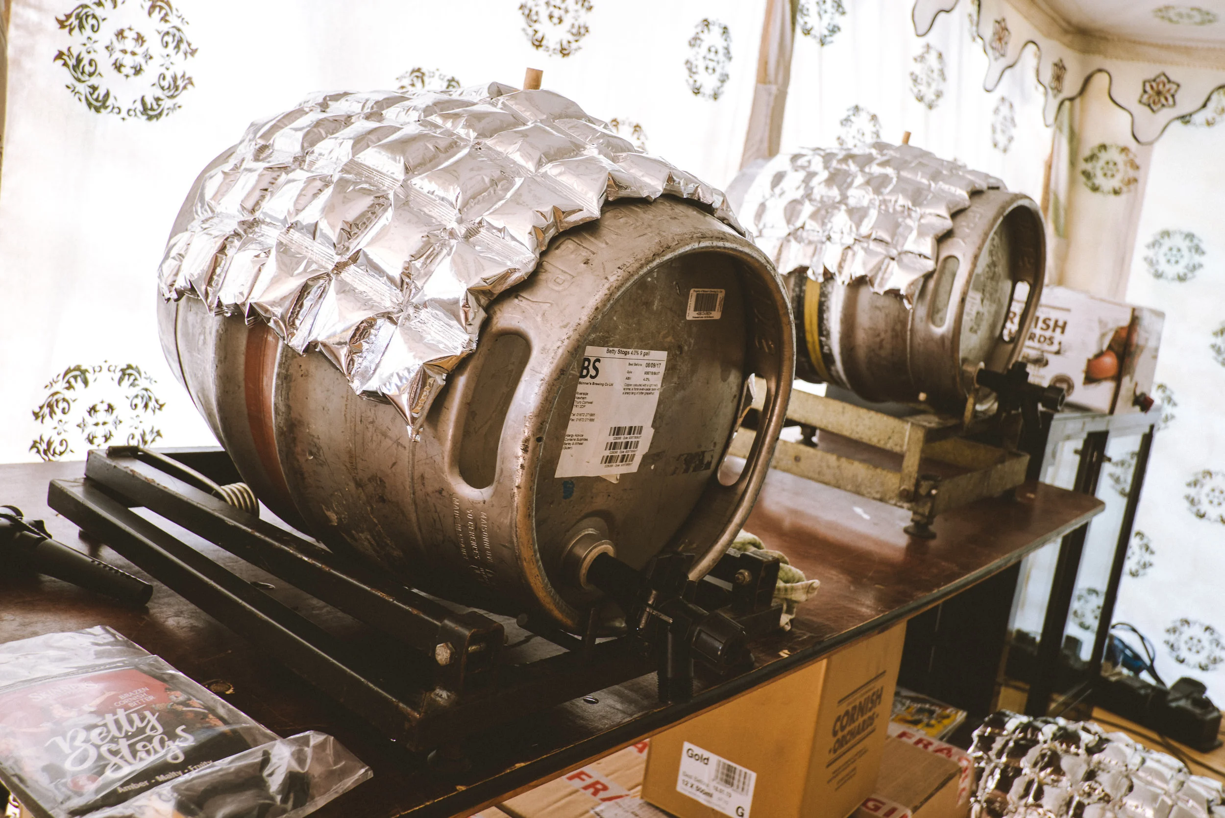 Two large candy or caramel apples wrapped in aluminum foil, mounted on machines for dipping or coating, on a wooden table.