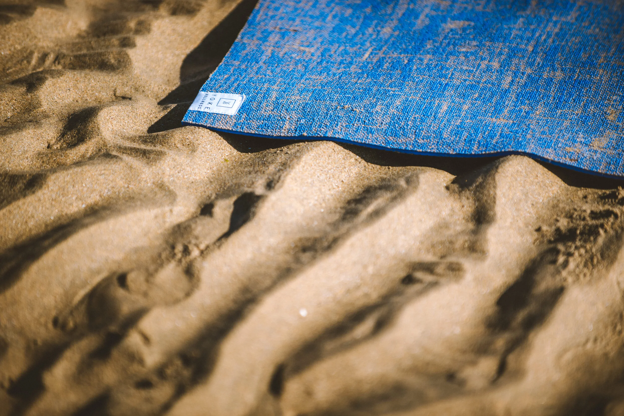 A blue patterned towel lying on sandy ground with visible footprints.