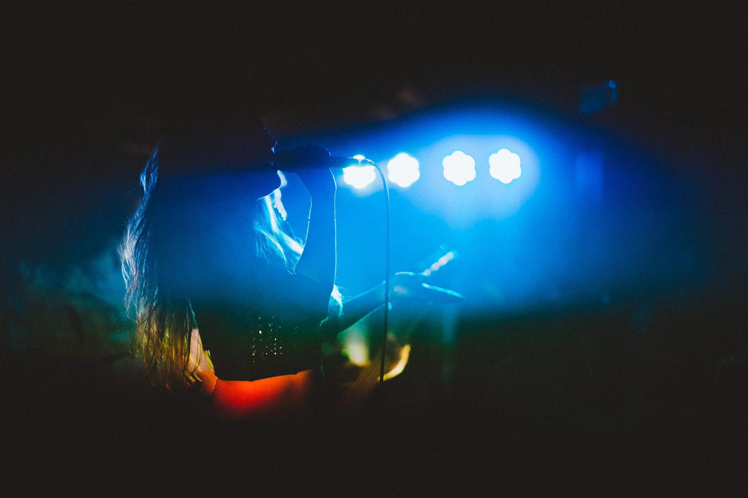 Silhouette of a woman singing into a microphone with blue stage lights in the background.