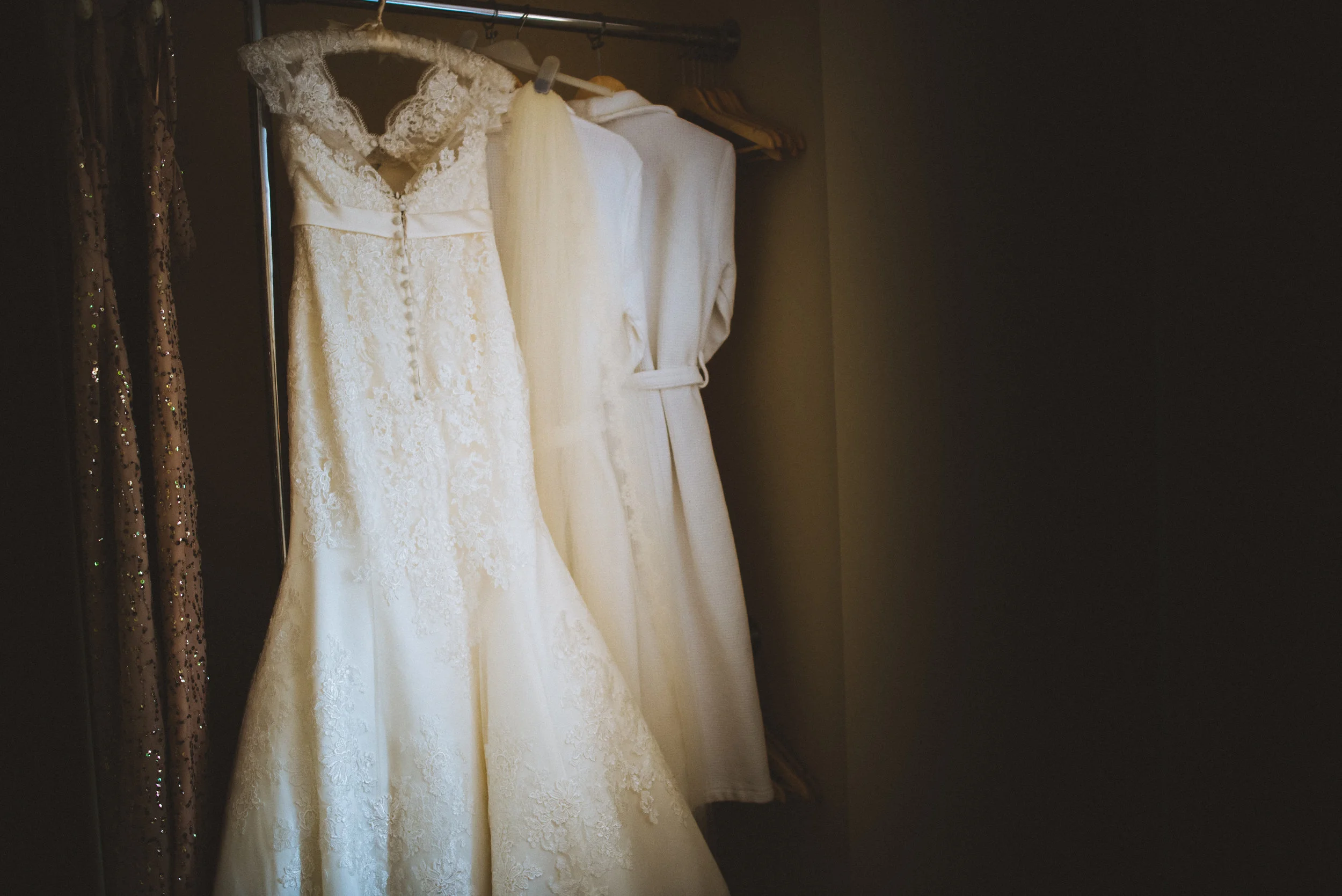 Wedding dresses hanging on a rack, including a lace wedding gown with buttons down the back.