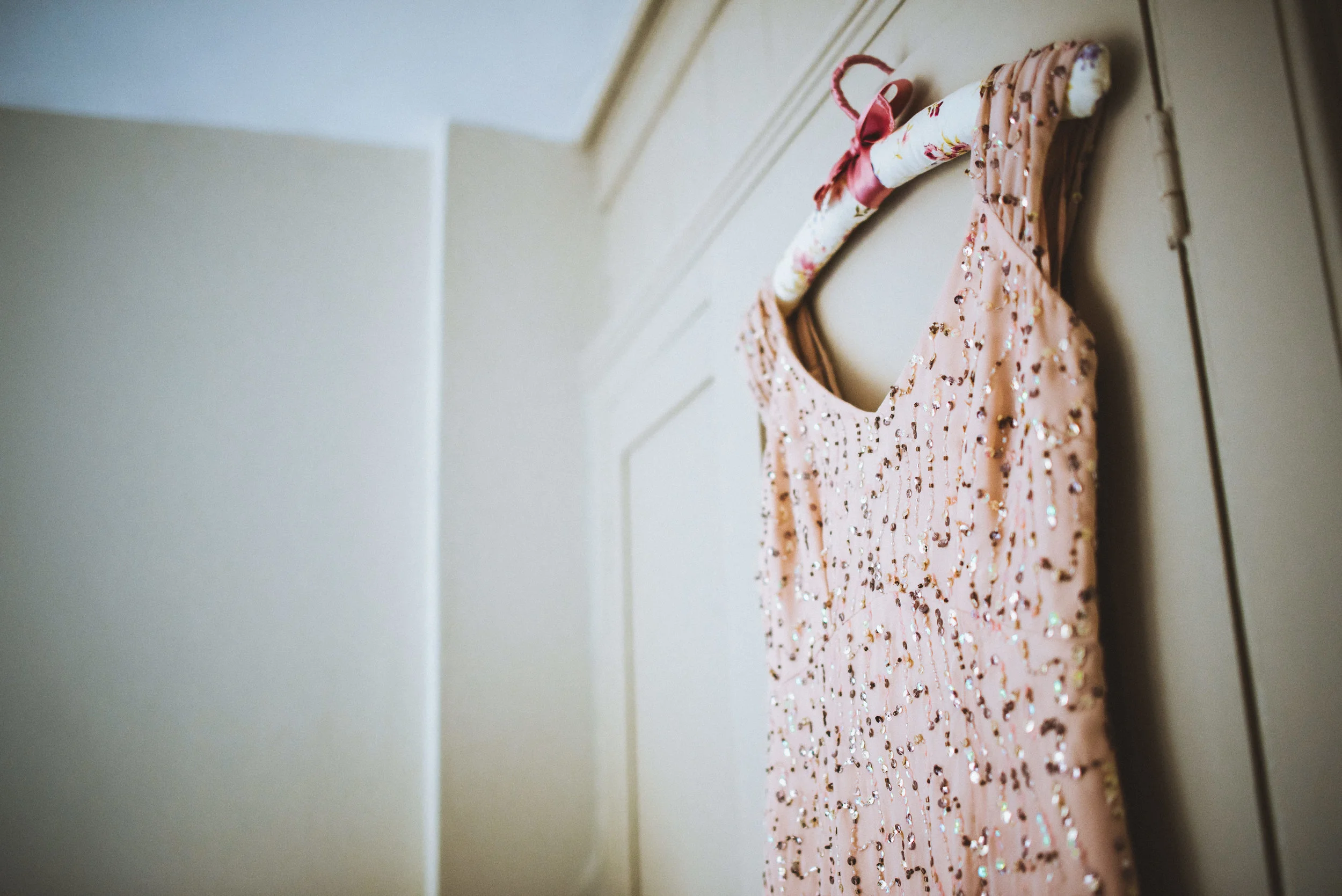 A pink dress with sequins hanging on a floral-patterned hanger on a white door.