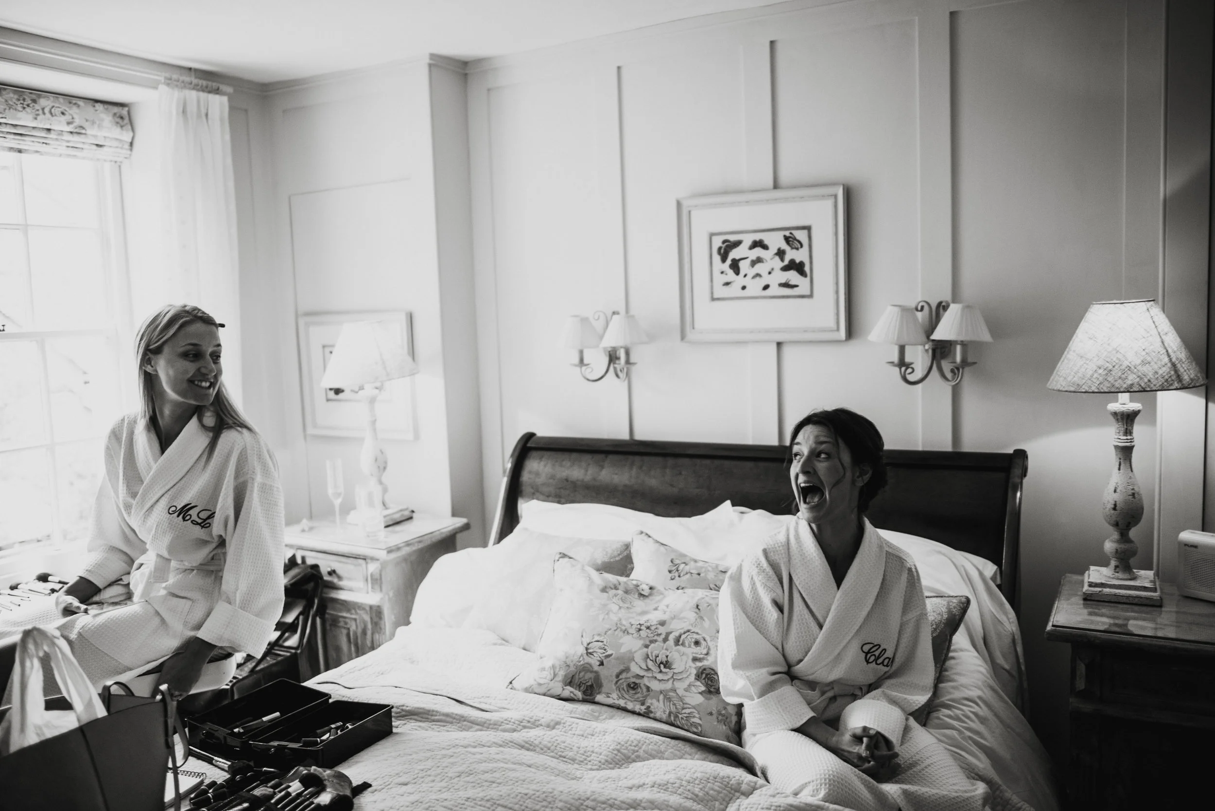 Isles of scilly photography. Two women in robes sitting on a bed in a well-lit room, one smiling and looking at the other, who is laughing with her mouth open.