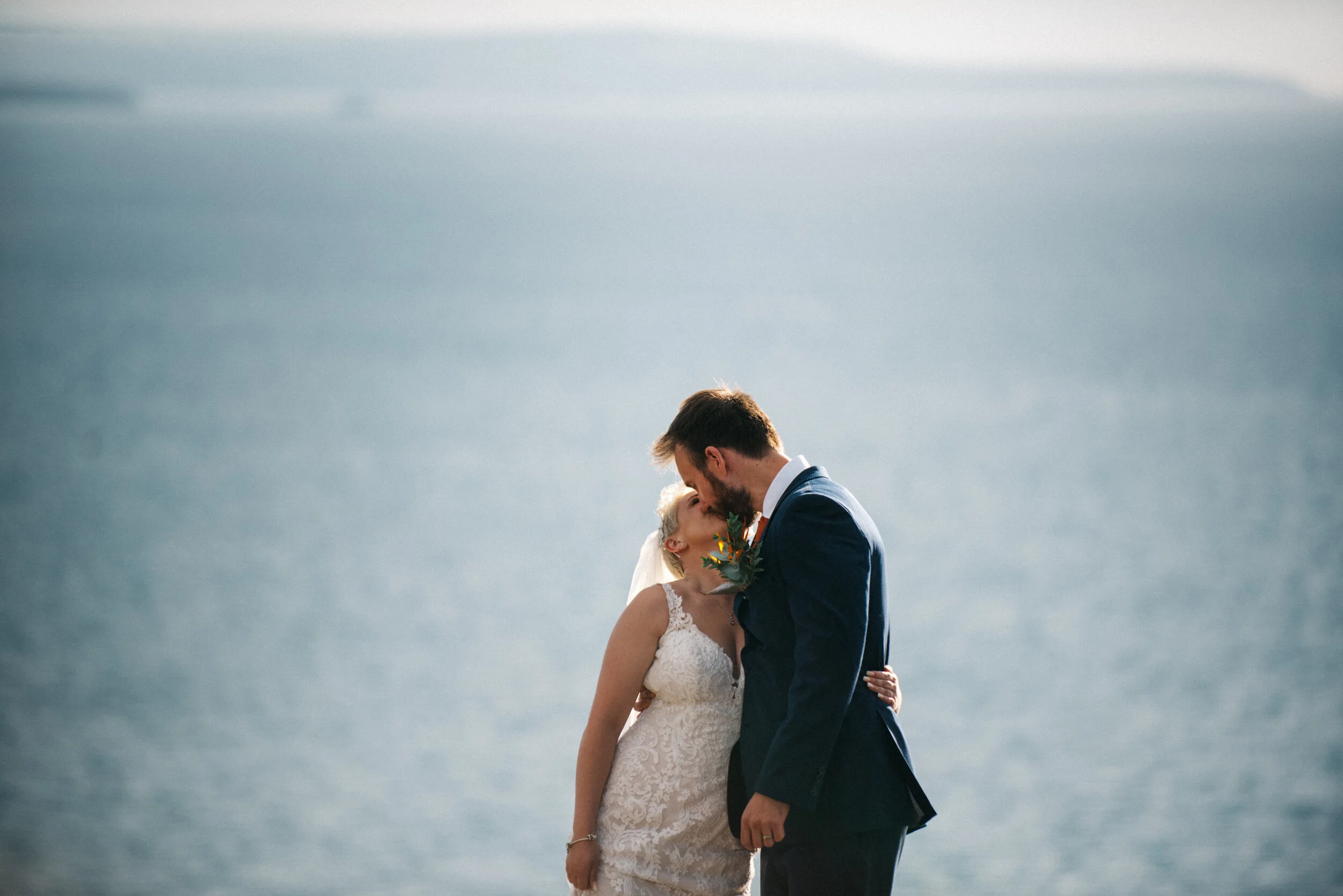 A bride and groom share a kiss near a body of water during their wedding.