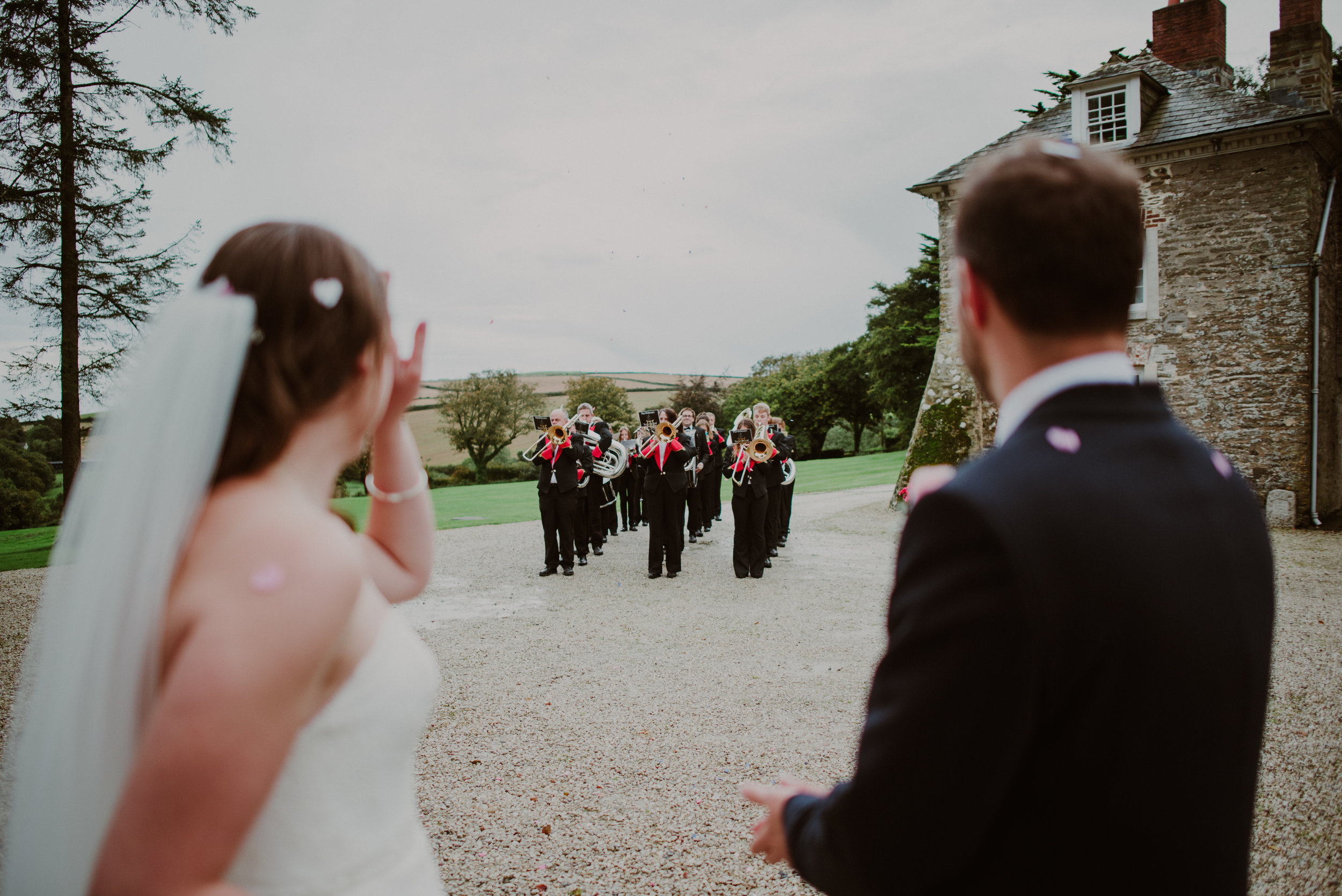 A bride and groom watching a marching band outdoors at a wedding ceremony.
