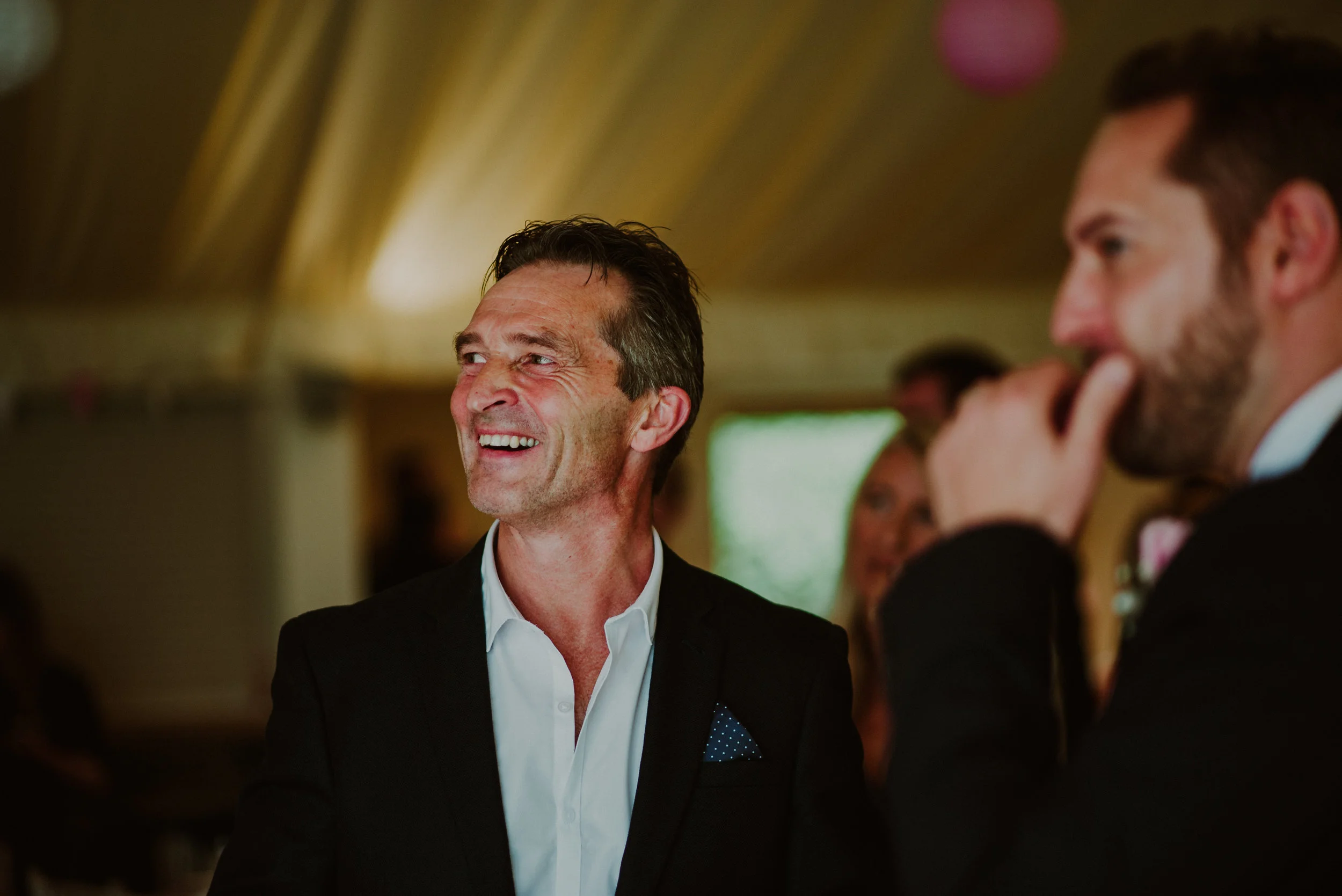 Smiling man in a suit at a social gathering with others in the background.